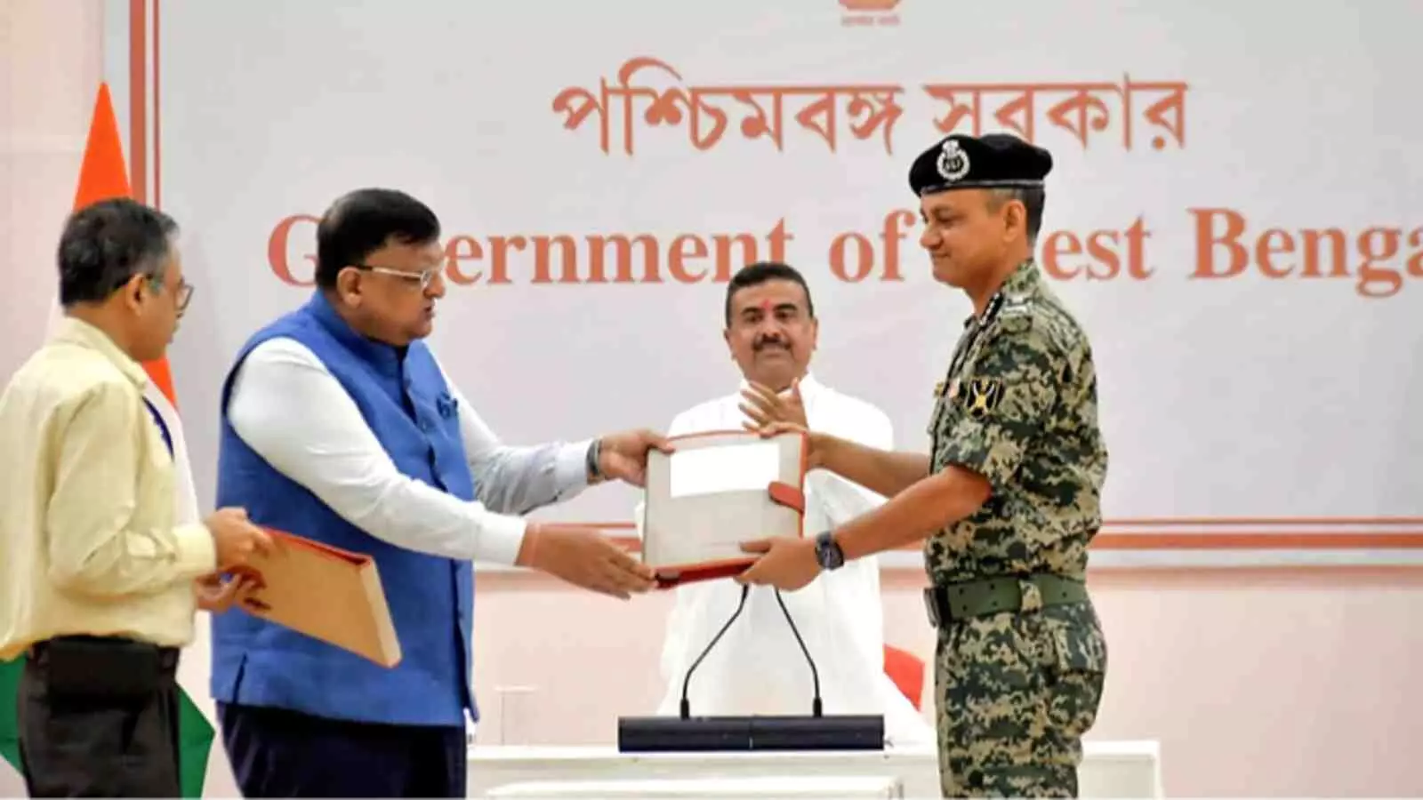 सचिवालय में अधिकारी बीएसएफ सुरक्षाकर्मी को भारत बांग्लादेश सीमा बाड़बंदी के दस्तावेज सौंपते हुए मुद्रित पृष्ठभूमि के सामने खड़े हैं।
