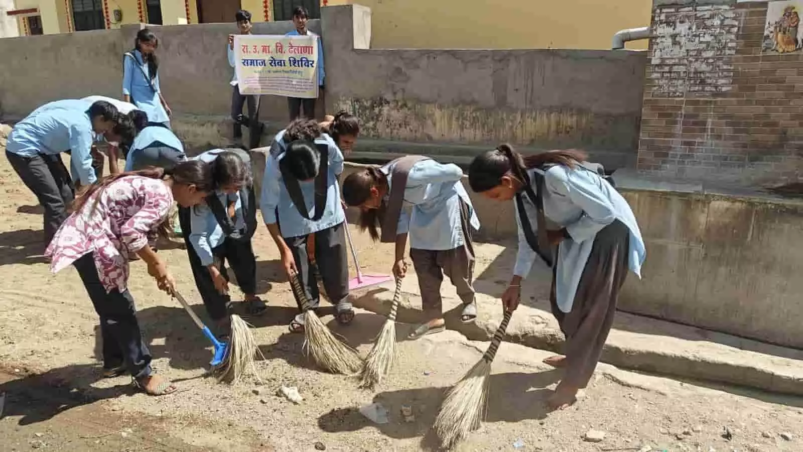 झाड़ू और फावड़े से जमीन साफ करते हुए स्कूल यूनिफॉर्म पहने छात्र-छात्राएं ढेलाणा में समाज सेवा शिविर के दौरान। झाड़ू और फावड़े से जमीन साफ करते हुए स्कूल यूनिफॉर्म पहने छात्र-छात्राएं ढेलाणा में समाज सेवा शिविर के दौरान।