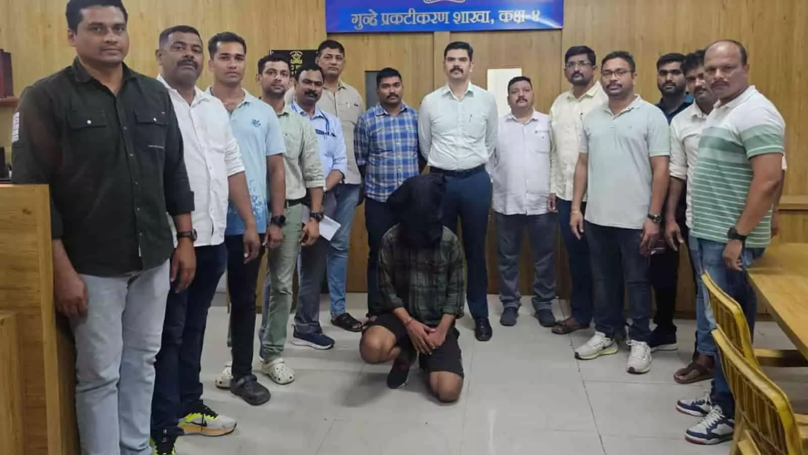 क्राइम ब्रांच कार्यालय में पुलिस अधिकारियों के बीच घुटने के बल बैठा मुंह ढका हुआ मर्डर का आरोपी।