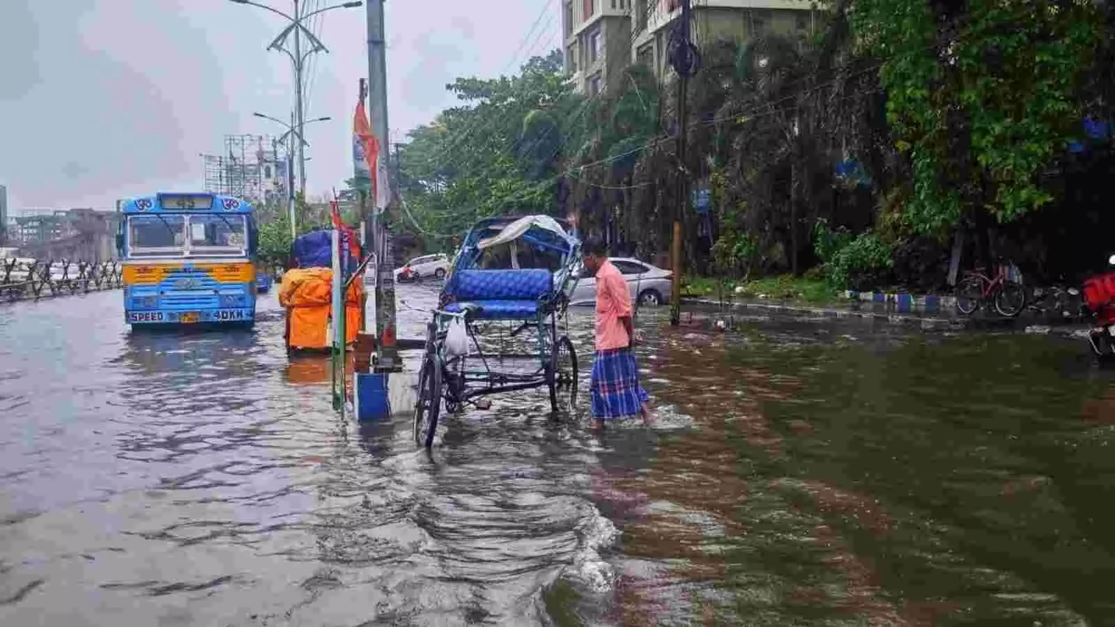 जलभराव वाली सड़क पर एक नीली बस और एक व्यक्ति रिक्शा खींचता हुआ दिखाई दे रहा है। जलभराव वाली सड़क पर एक नीली बस और एक व्यक्ति रिक्शा खींचता हुआ दिखाई दे रहा है।