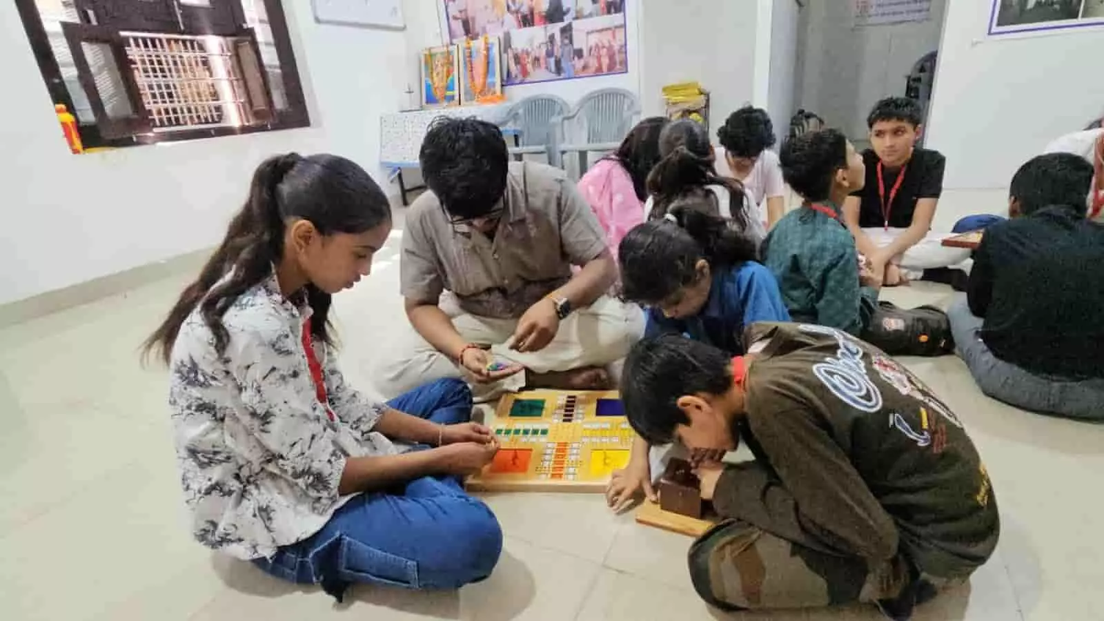 कमरे में फर्श पर बैठकर विशेष रूप से निर्मित लूडो बोर्ड पर गेम खेलते हुए दिव्यांग बच्चे और शिक्षक। कमरे में फर्श पर बैठकर विशेष रूप से निर्मित लूडो बोर्ड पर गेम खेलते हुए दिव्यांग बच्चे और शिक्षक।