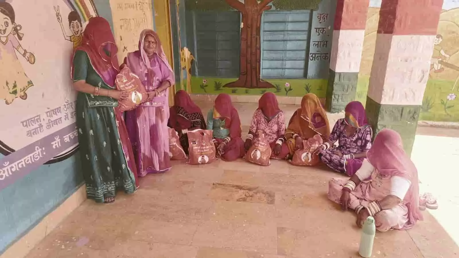 आंगनबाड़ी केंद्र परिसर में महिलाओं को मुख्यमंत्री सुपोषण न्यूट्री किट वितरित करती कार्यकर्ता और बैठी हुई लाभार्थी महिलाएं।