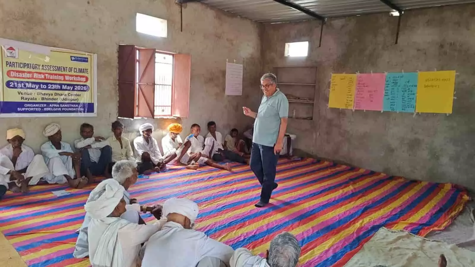 रायला में जलवायु परिवर्तन कार्यशाला के दौरान दीवार पर लगे फसल चार्ट के सामने बैठे किसान और जानकारी देते प्रशिक्षक रायला में जलवायु परिवर्तन कार्यशाला के दौरान दीवार पर लगे फसल चार्ट के सामने बैठे किसान और जानकारी देते प्रशिक्षक