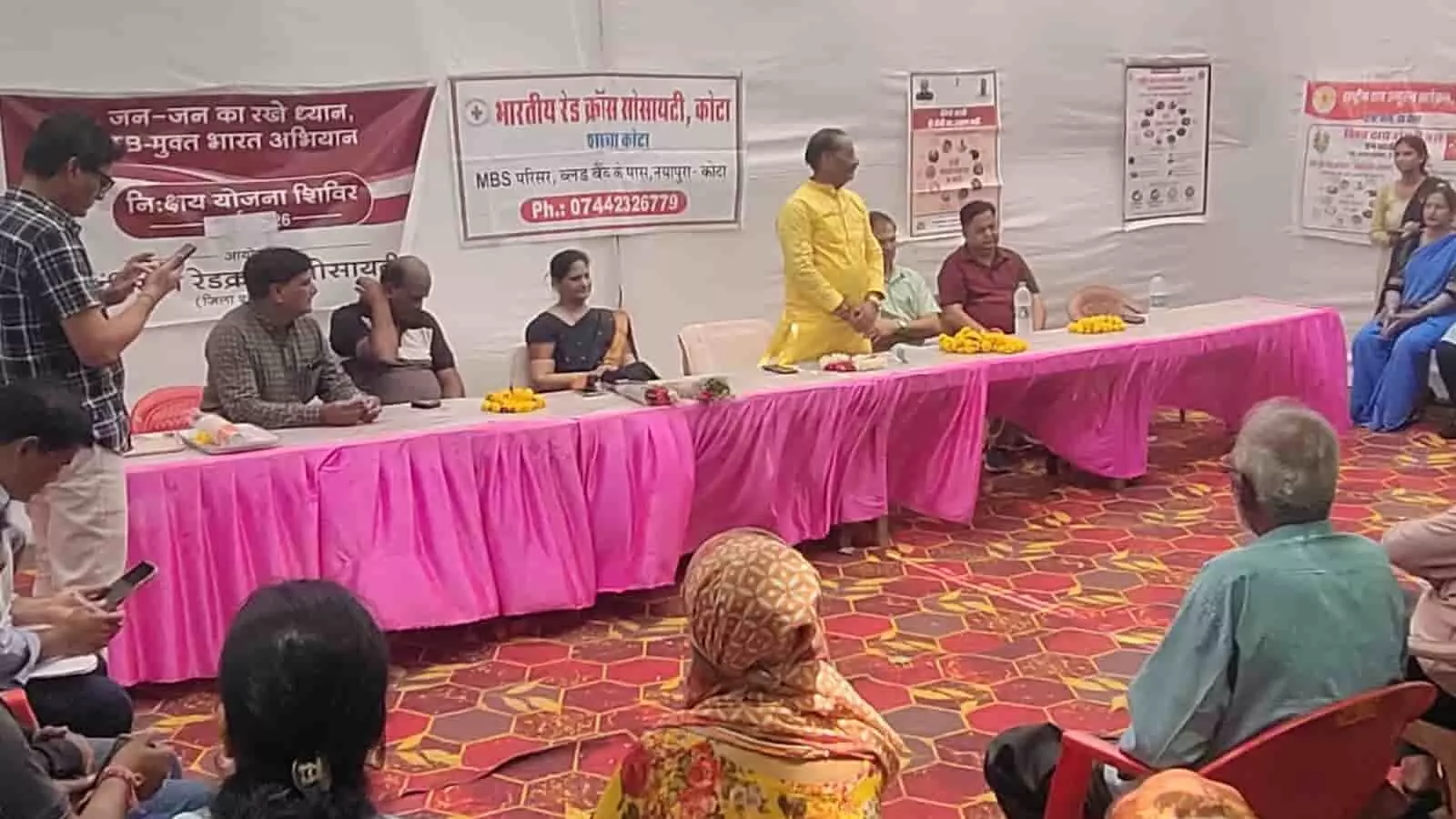 कोटा के स्वास्थ्य केंद्र में रेड क्रॉस सोसायटी के निक्षय योजना शिविर मंच पर बैठे अतिथि और सामने उपस्थित नागरिक। कोटा के स्वास्थ्य केंद्र में रेड क्रॉस सोसायटी के निक्षय योजना शिविर मंच पर बैठे अतिथि और सामने उपस्थित नागरिक।