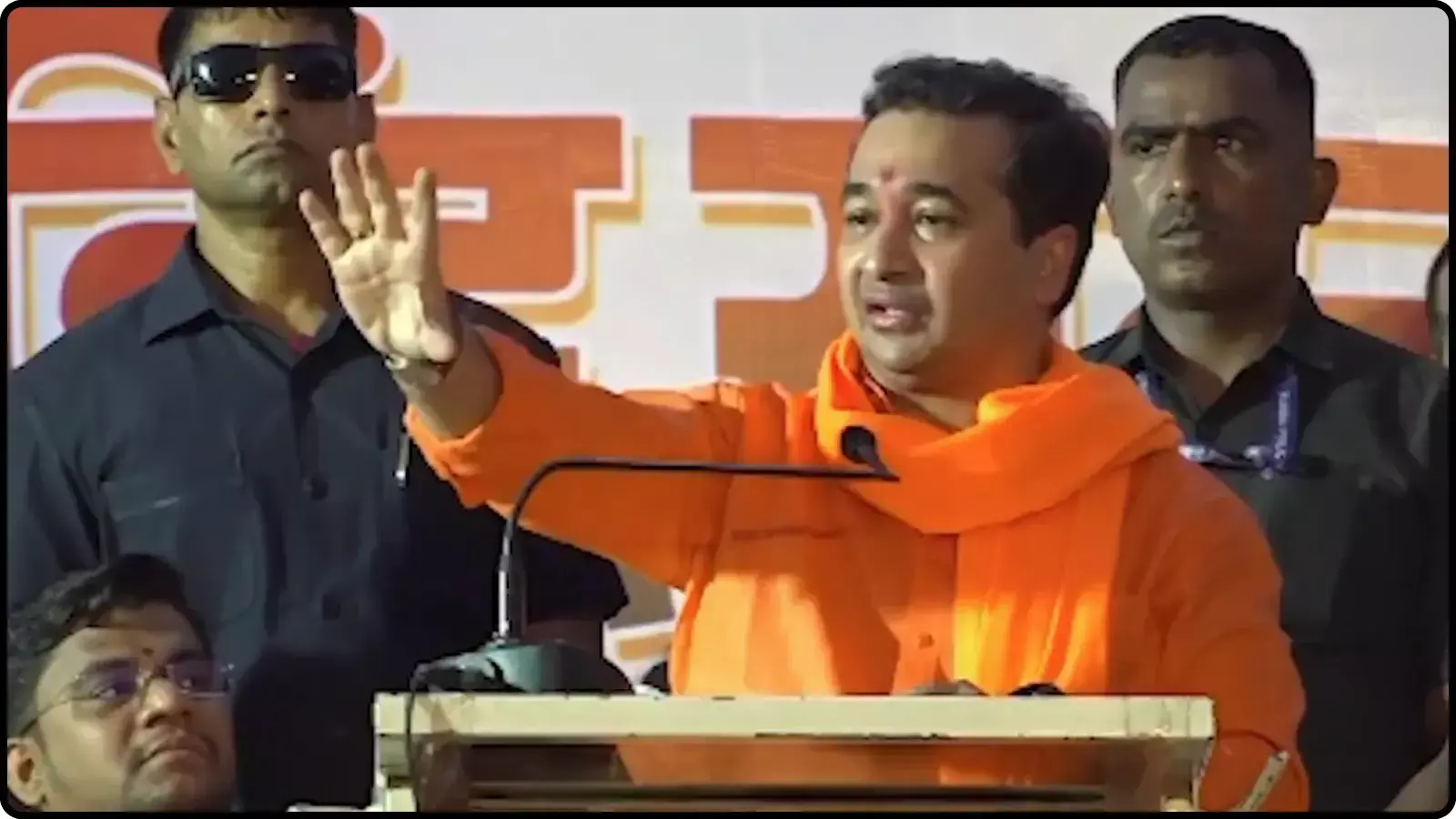 मंच पर पोडियम के पीछे खड़े होकर हाथ उठाकर भाषण देते हुए नेता नितेश राणे। मंच पर पोडियम के पीछे खड़े होकर हाथ उठाकर भाषण देते हुए नेता नितेश राणे।