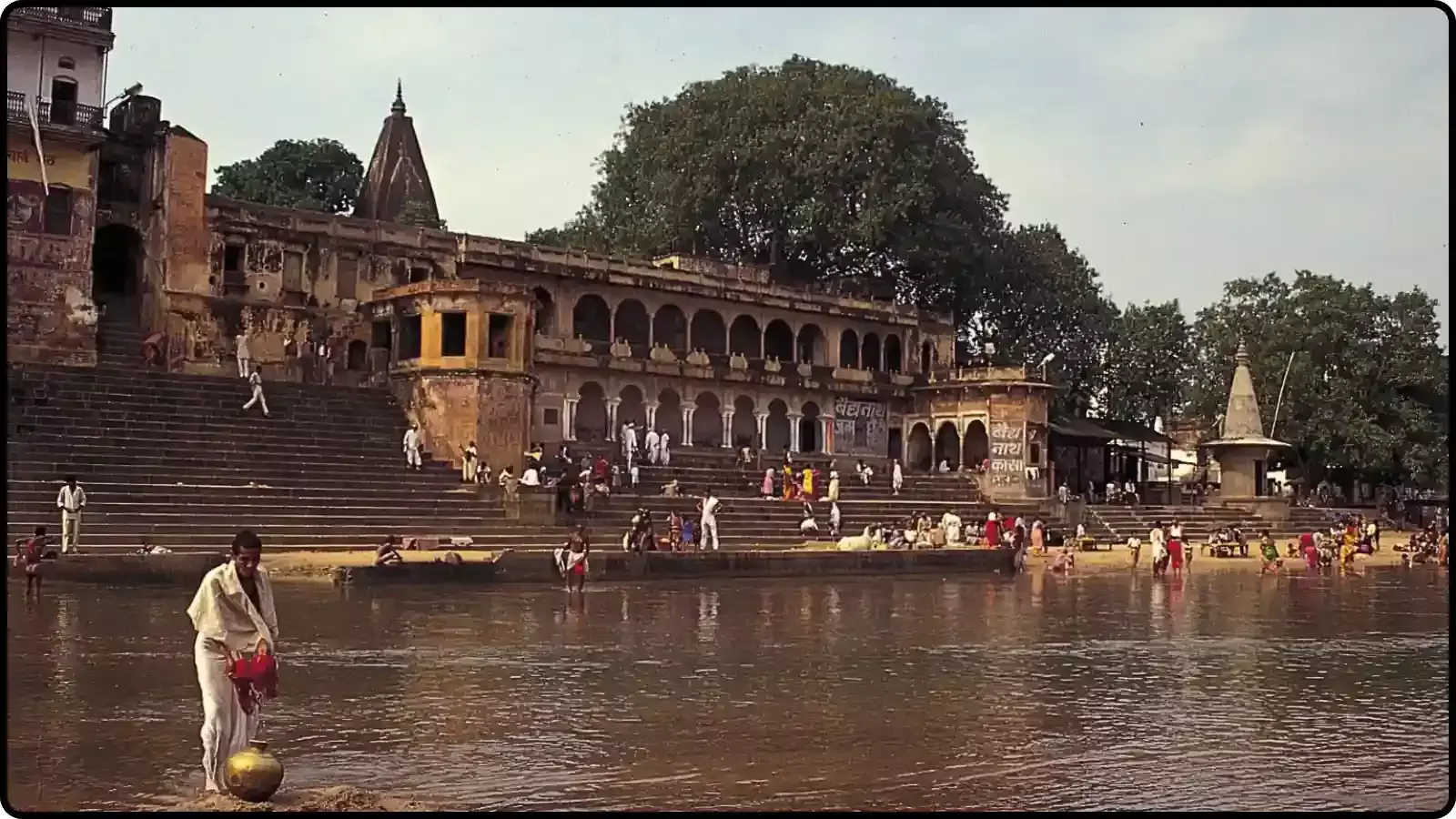 नदी के किनारे बना हुआ पुराना घाट और ऐतिहासिक इमारत जहां कुछ लोग पानी में खड़े हैं। नदी के किनारे बना हुआ पुराना घाट और ऐतिहासिक इमारत जहां कुछ लोग पानी में खड़े हैं।