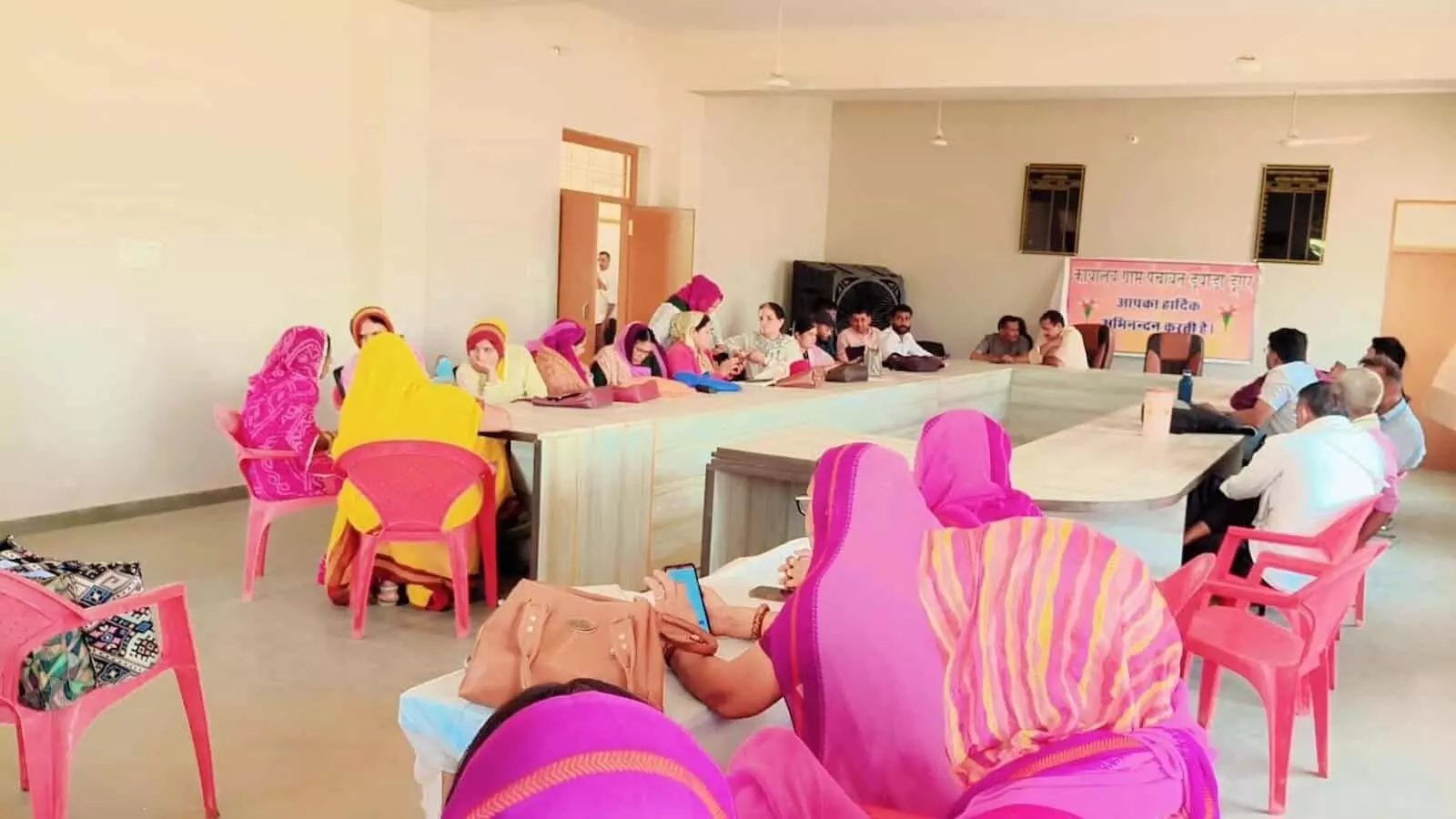 ग्राम पंचायत कार्यालय के सभागार में बैठे प्रशासनिक अधिकारी और अग्रिम पंक्ति में बैठीं ग्रामीण महिलाएं।