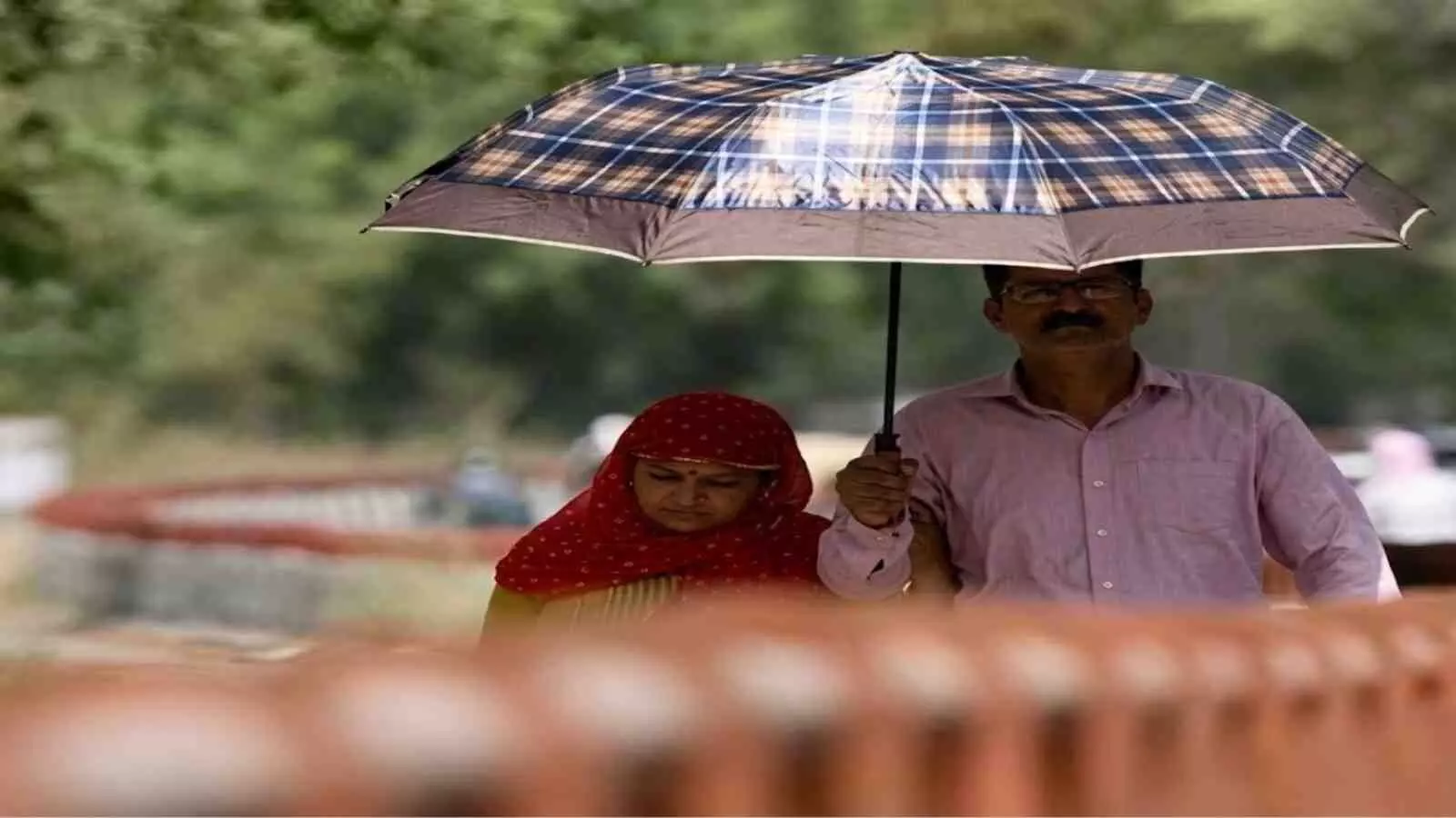 धूप से बचने के लिए एक पुरुष और महिला छाता पकड़कर सड़क पर चलते हुए राजस्थान में भीषण लू के संदर्भ में दिख रहे हैं। धूप से बचने के लिए एक पुरुष और महिला छाता पकड़कर सड़क पर चलते हुए राजस्थान में भीषण लू के संदर्भ में दिख रहे हैं।