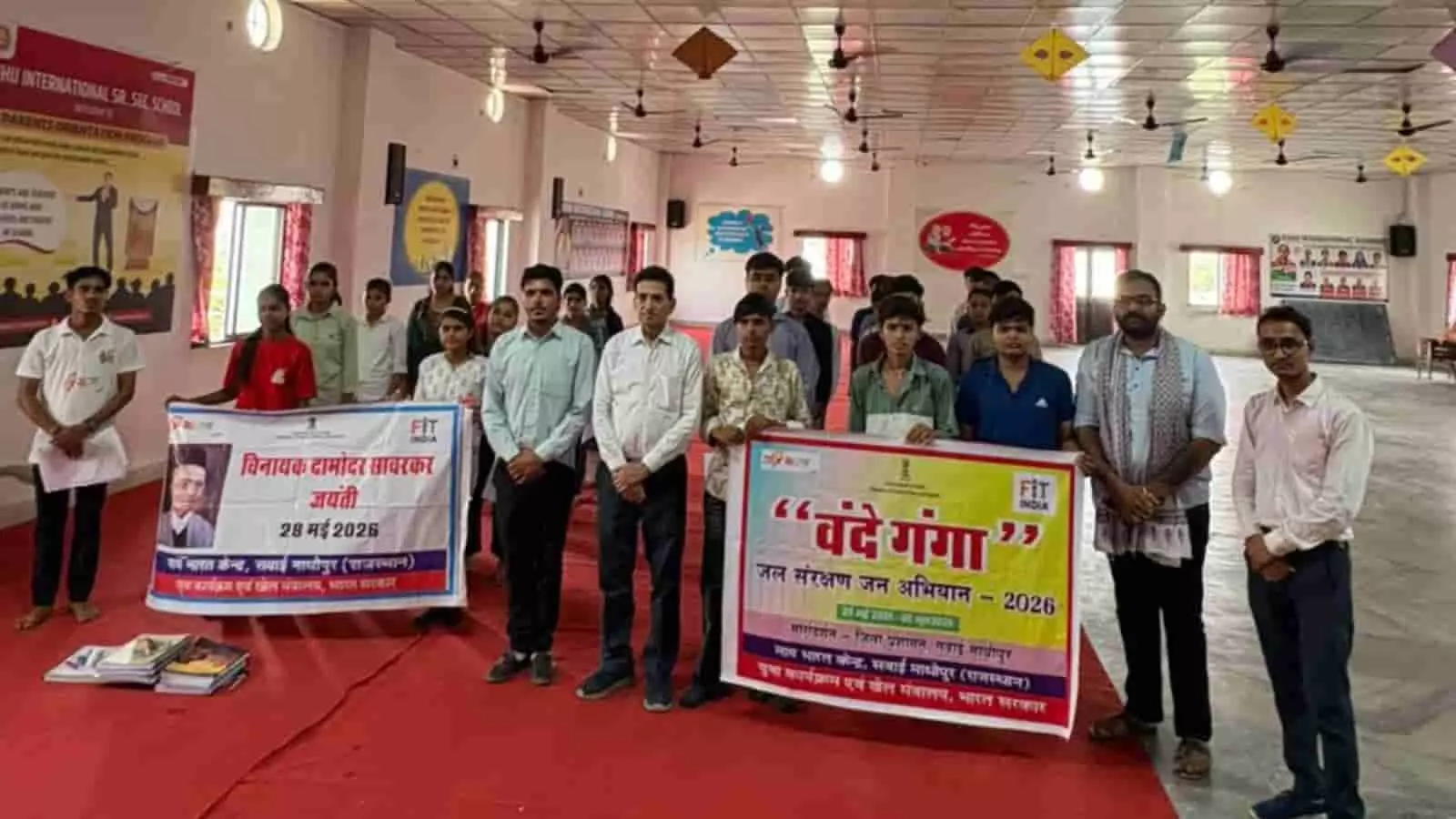 सवाई माधोपुर के कुहू फाउंडेशन परिसर में बैनर पकड़े खड़े लोग वीर सावरकर जयंती कार्यक्रम में शामिल हैं।