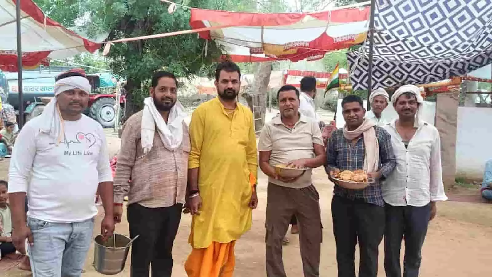 तपोभूमि आश्रम खेड़ा जमालपुर में भागवत कथा समापन पर भंडारे के दौरान पीली पोशाक पहने मुख्य व्यक्ति के साथ बर्तन थामे सेवादार खड़े हैं।