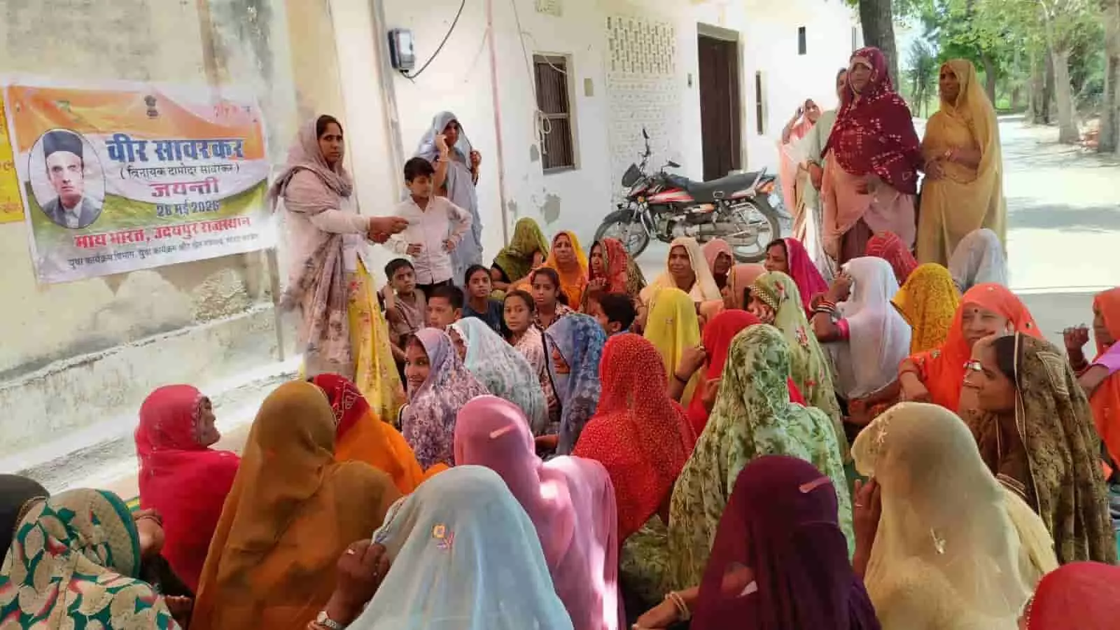उदयपुर के वासनी कला में वीर सावरकर जयंती कार्यक्रम के बैनर के पास बैठीं ग्रामीण महिलाएं। उदयपुर के वासनी कला में वीर सावरकर जयंती कार्यक्रम के बैनर के पास बैठीं ग्रामीण महिलाएं।