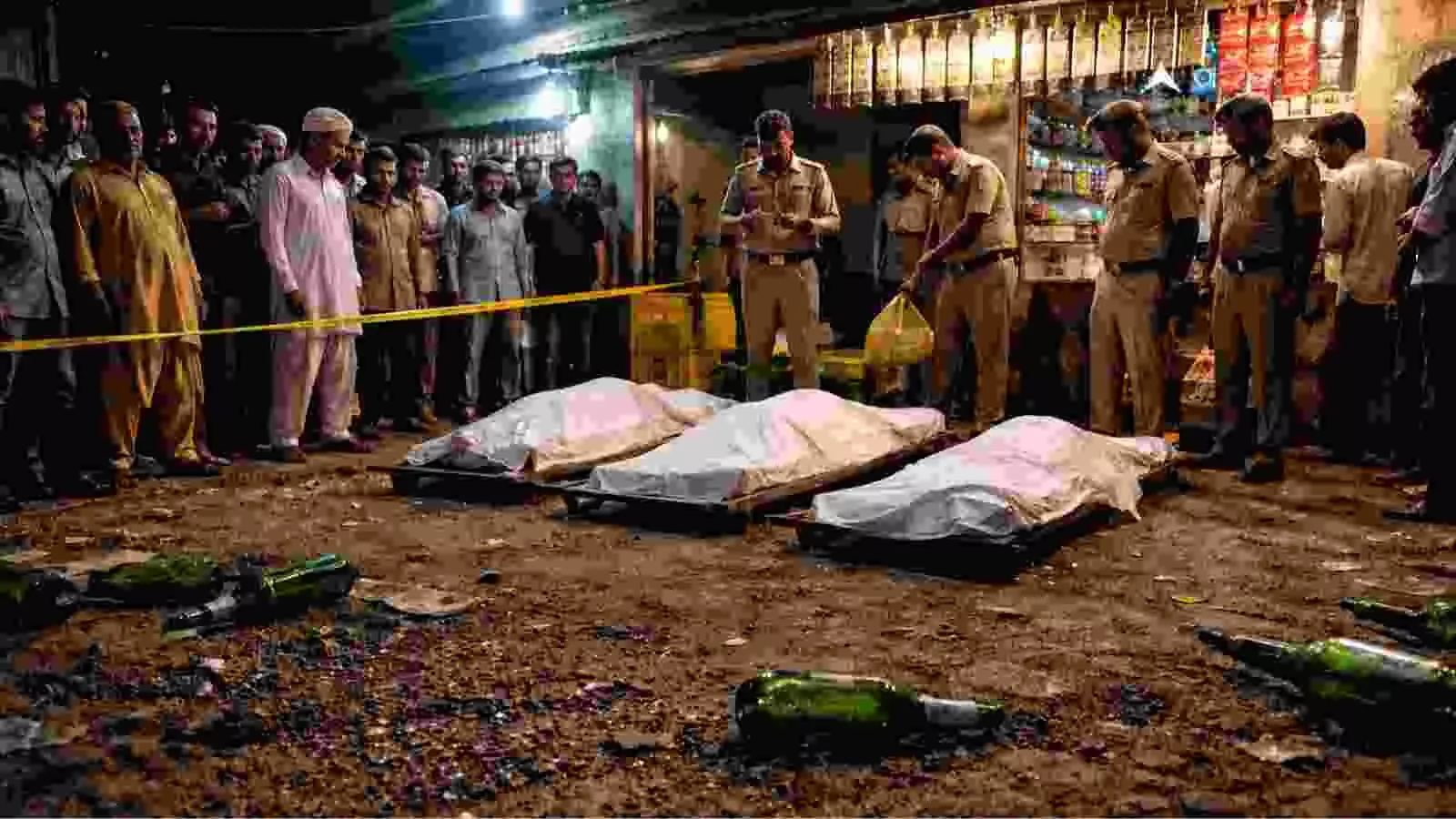 जमीन पर पड़ी कांच की बोतलें और सफेद कफन से ढके शवों के पास खड़े पुलिसकर्मी।
