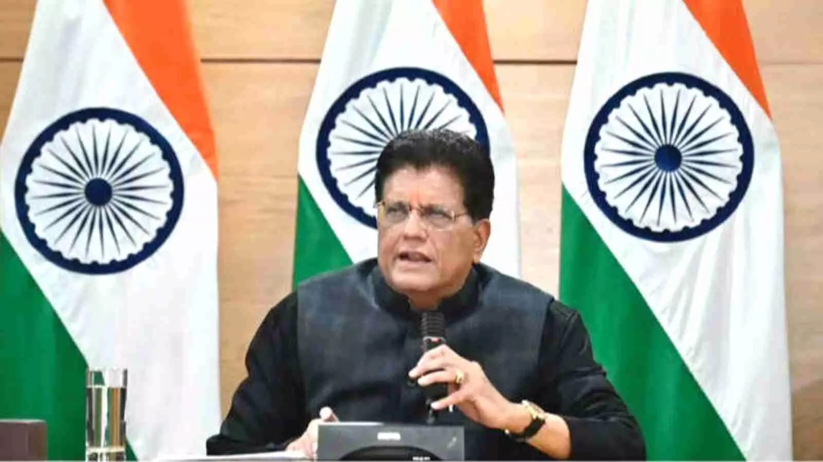 तीन भारतीय तिरंगे झंडों के सामने काले रंग के कुर्ते में बैठकर माइक थामे भाषण देते हुए एक भारतीय पुरुष मंत्री। तीन भारतीय तिरंगे झंडों के सामने काले रंग के कुर्ते में बैठकर माइक थामे भाषण देते हुए एक भारतीय पुरुष मंत्री।