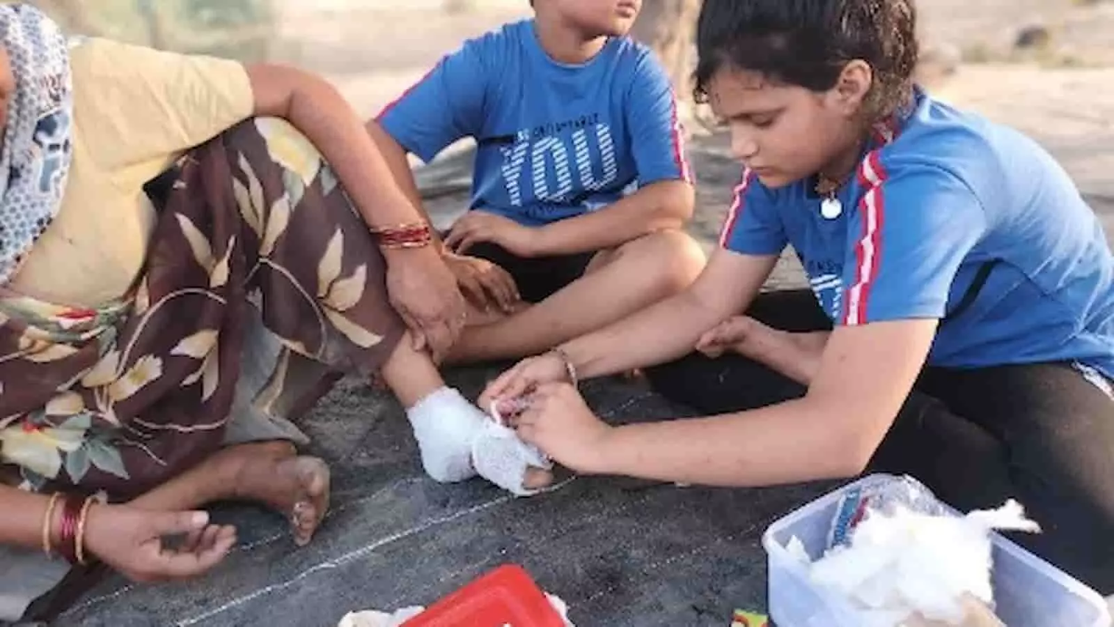 मैदान में बैठी बच्ची द्वारा बुजुर्ग महिला के पैर में प्राथमिक उपचार की पट्टी बांधी जा रही है। मैदान में बैठी बच्ची द्वारा बुजुर्ग महिला के पैर में प्राथमिक उपचार की पट्टी बांधी जा रही है।