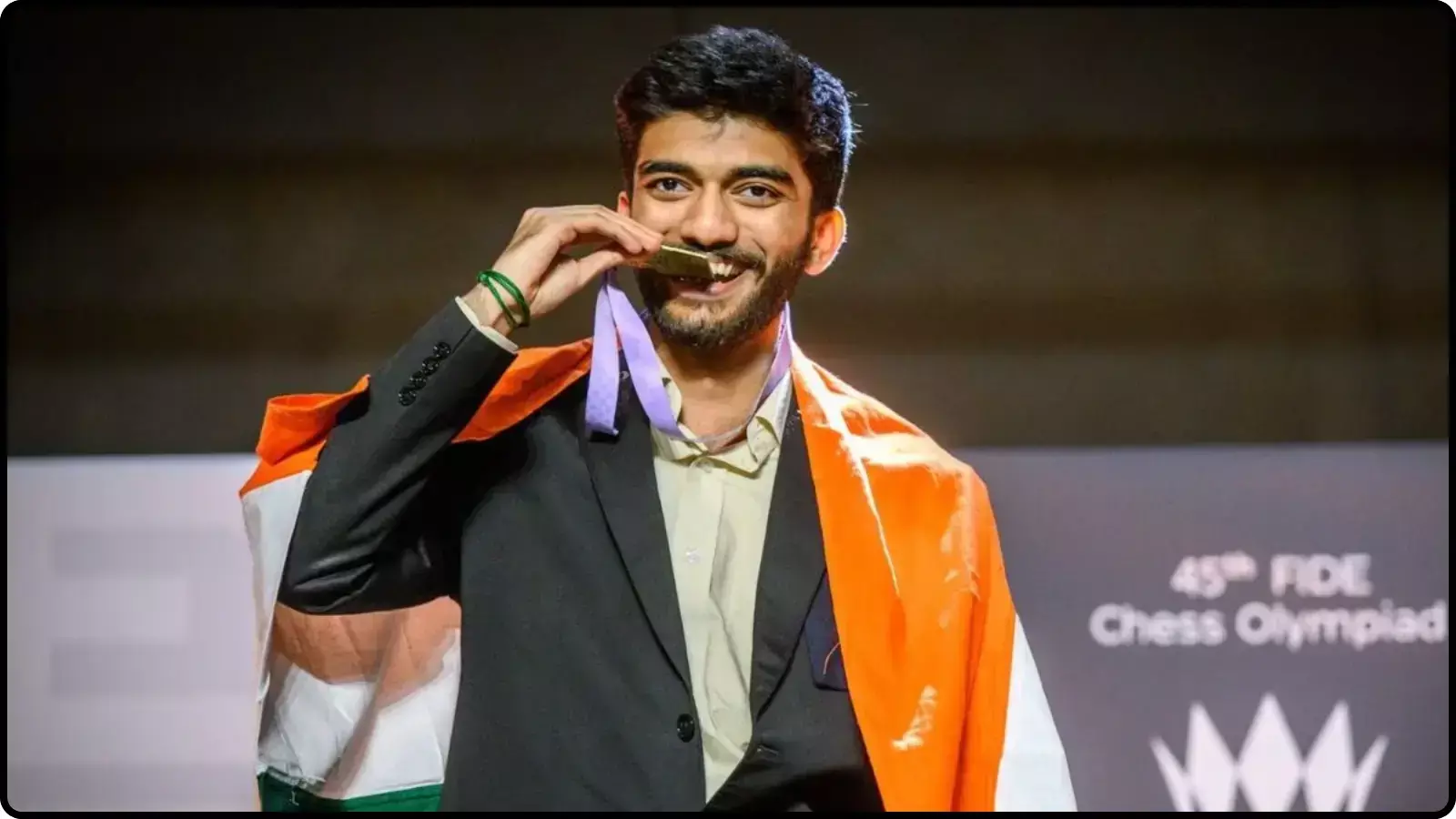 मंच पर गले में पदक और कंधे पर तिरंगा लपेटे मुस्कुराते हुए खड़े शतरंज खिलाड़ी डी गुकेश।