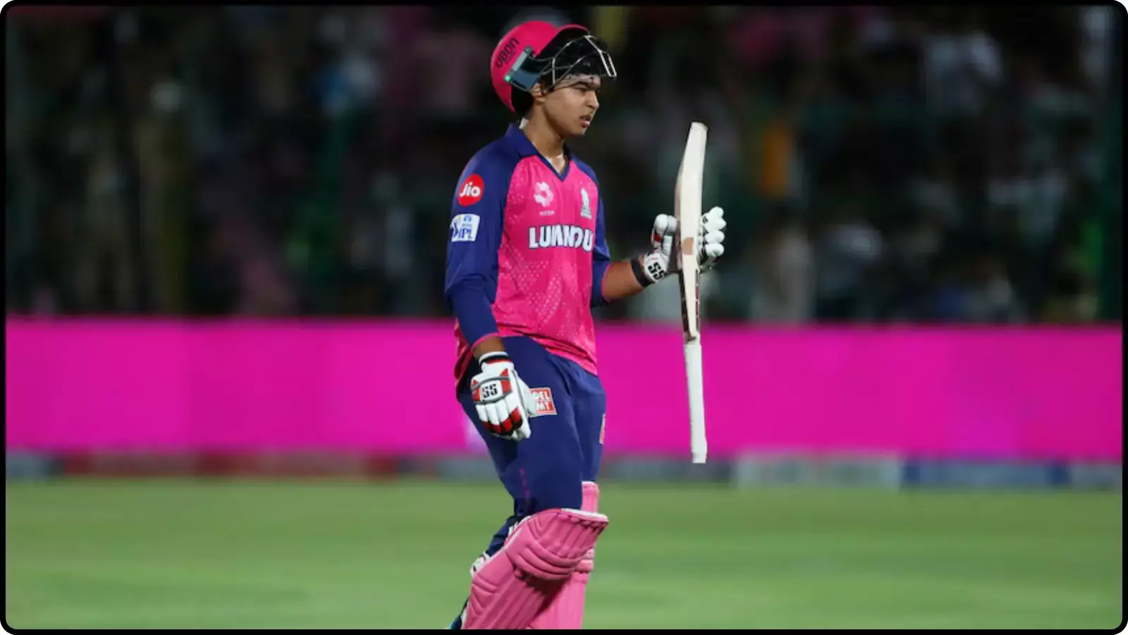 क्रिकेट मैदान पर पिंक जर्सी और हेलमेट पहने हाथ में बल्ला लेकर चलते हुए क्रिकेटर वैभव सूर्यवंशी।
