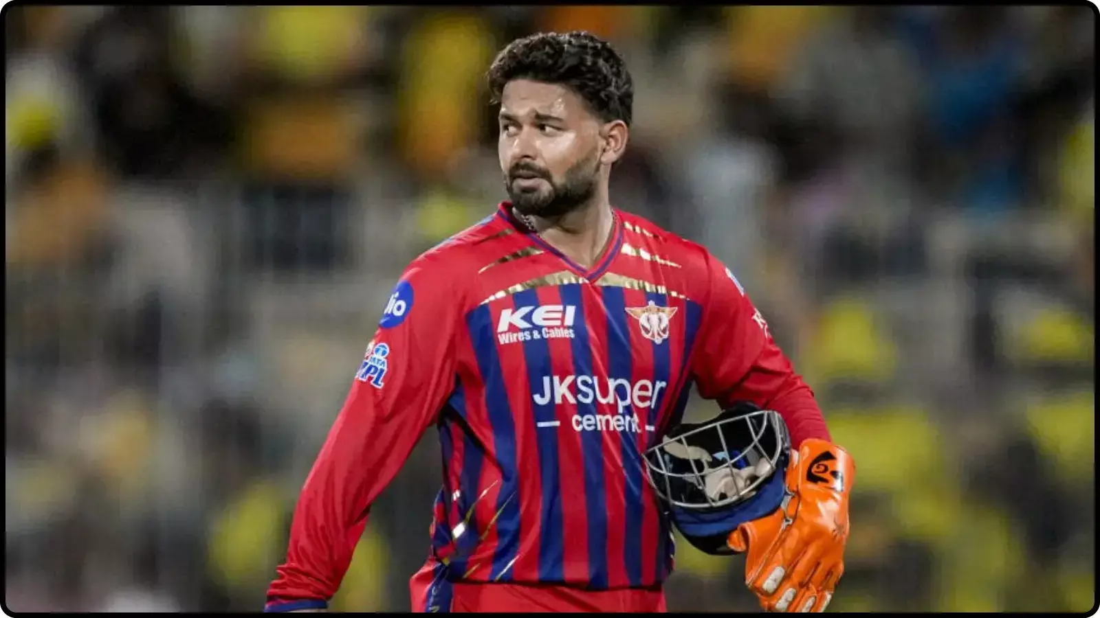 क्रिकेट मैदान पर लाल जर्सी पहने और हाथ में हेलमेट व ग्लव्स पकड़े खड़े क्रिकेटर ऋषभ पंत।