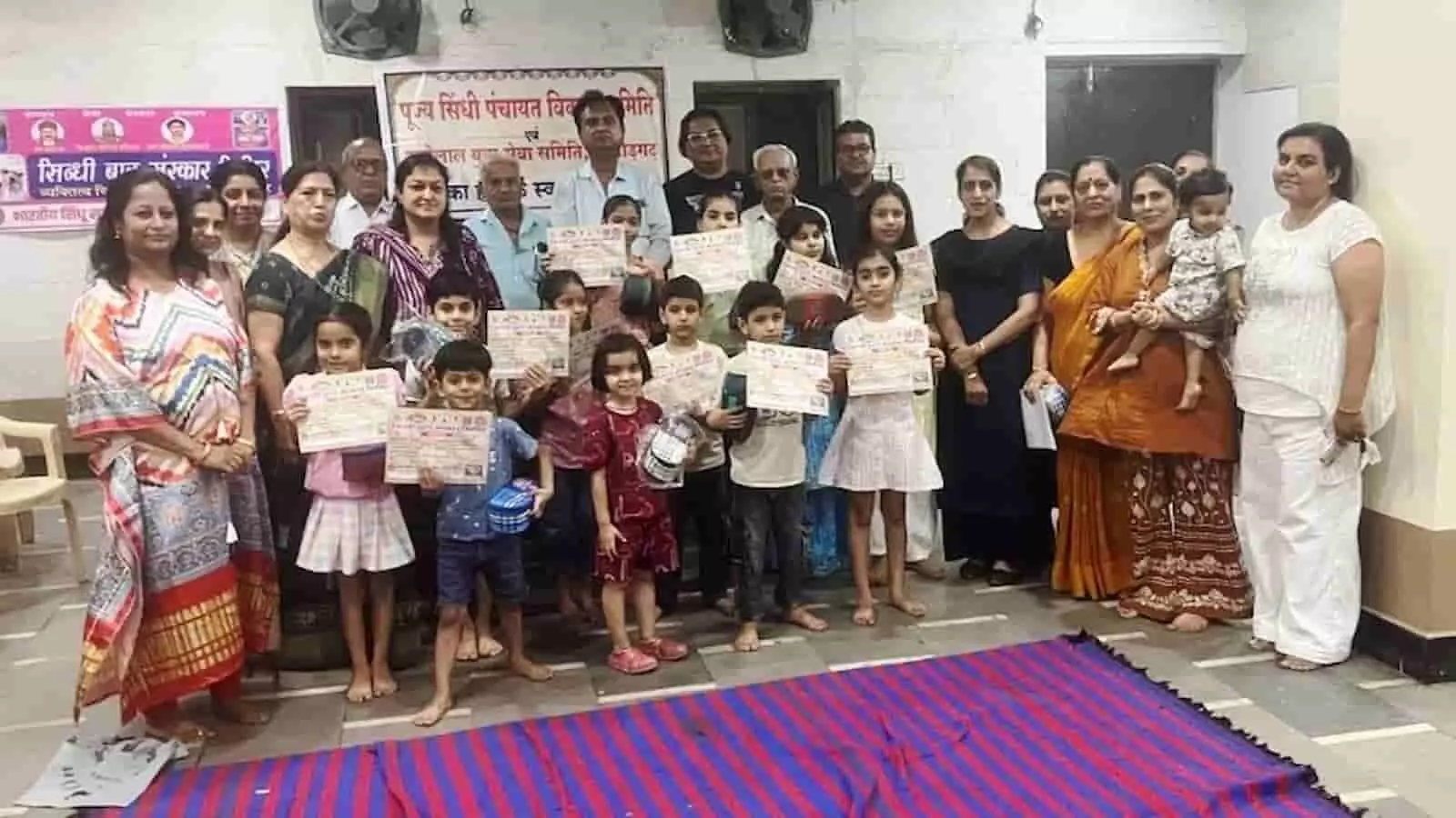 सिंधु कम्यूनिटी हॉल में प्रमाण पत्र और उपहार हाथ में लिए खड़े बच्चे और अतिथि बाल संस्कार शिविर समापन के दौरान