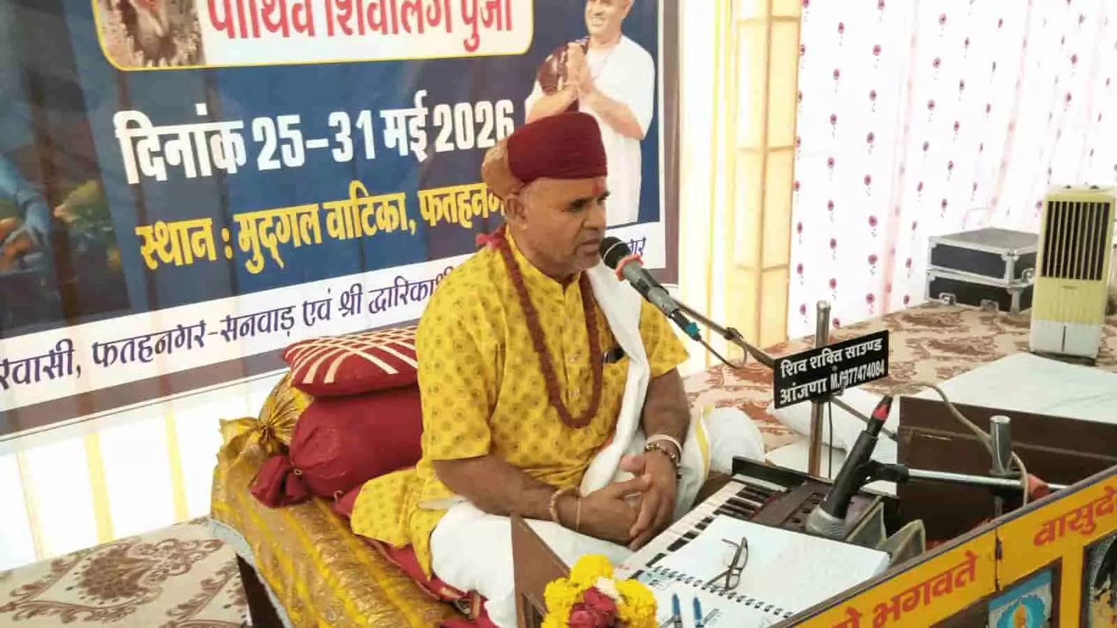 मुद्द्गल वाटिका फतहनगर में व्यासपीठ पर बैठकर माइक के सामने शिव महापुराण कथा का वाचन करते पंडित माणक