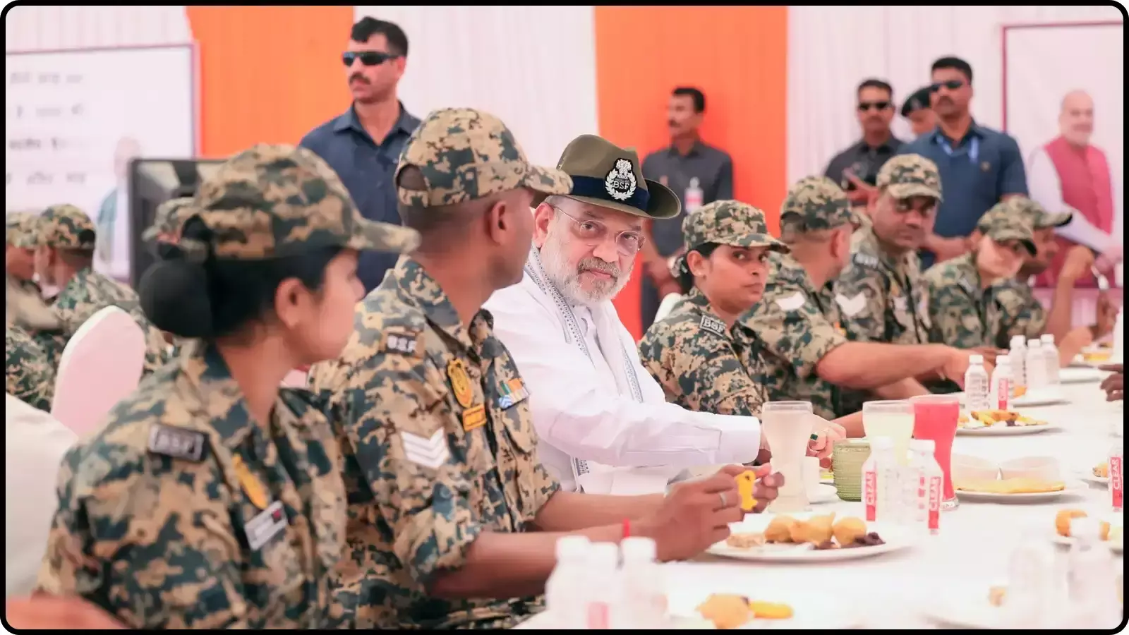 भोजन की मेज पर बीएसएफ जवानों के बीच बैठे और सिर पर टोपी पहने केंद्रीय गृह मंत्री अमित शाह।