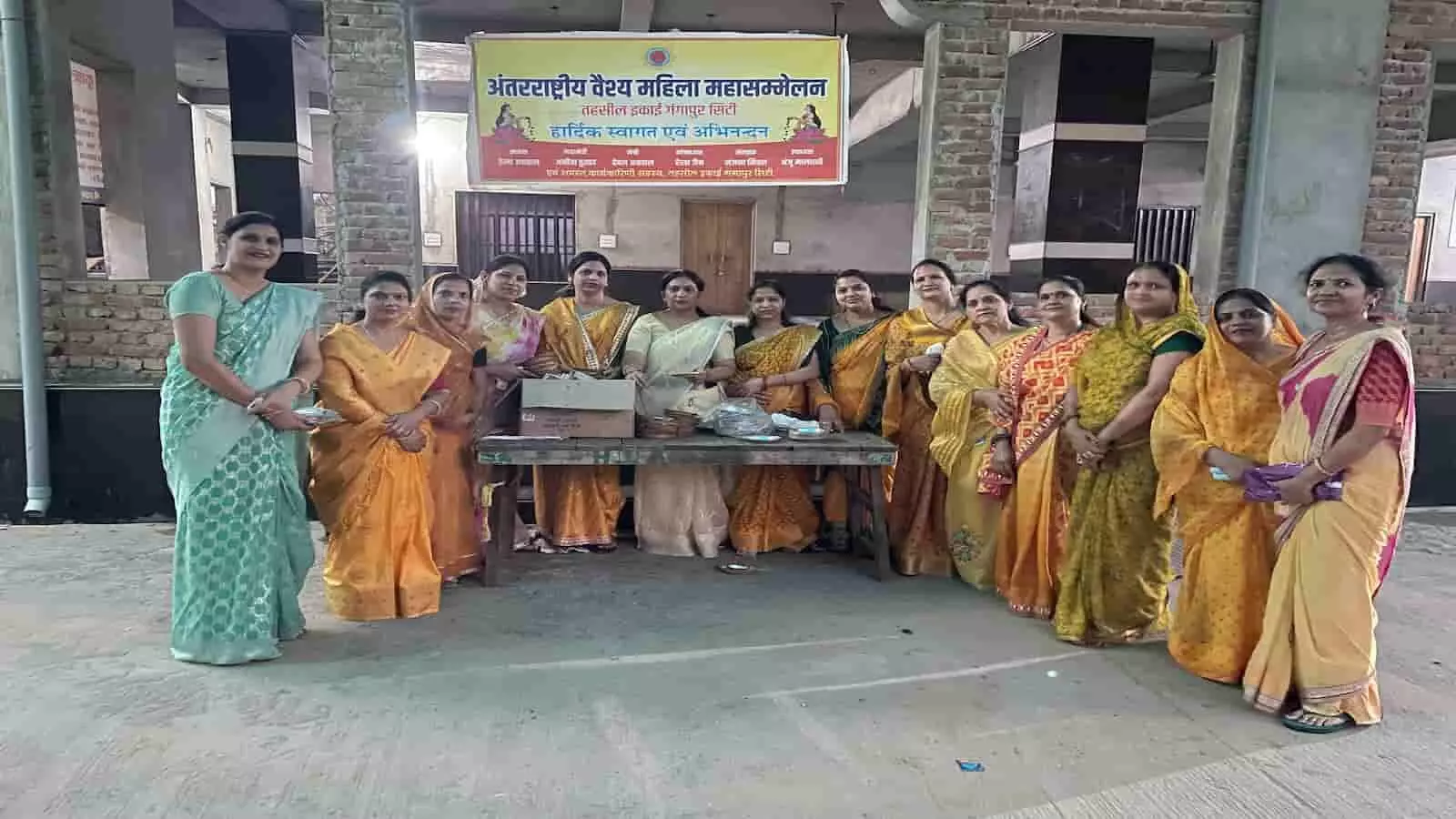 मंदिर परिसर में बैनर के सामने खड़ी अंतर्राष्ट्रीय वैश्य महिला महासम्मेलन की महिलाएं गंगापुर सिटी में प्रसादी वितरण कार्यक्रम के दौरान। मंदिर परिसर में बैनर के सामने खड़ी अंतर्राष्ट्रीय वैश्य महिला महासम्मेलन की महिलाएं गंगापुर सिटी में प्रसादी वितरण कार्यक्रम के दौरान।