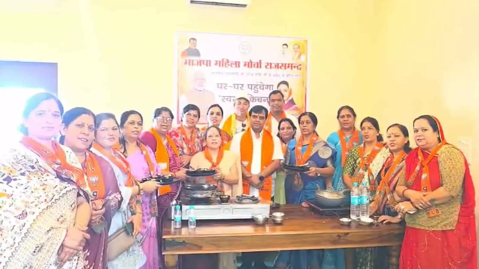 राजसमन्द में स्वस्थ किचन अभियान की बैठक के दौरान पोस्टर के पीछे खड़े भाजपा नेता और महिला मोर्चा पदाधिकारी।