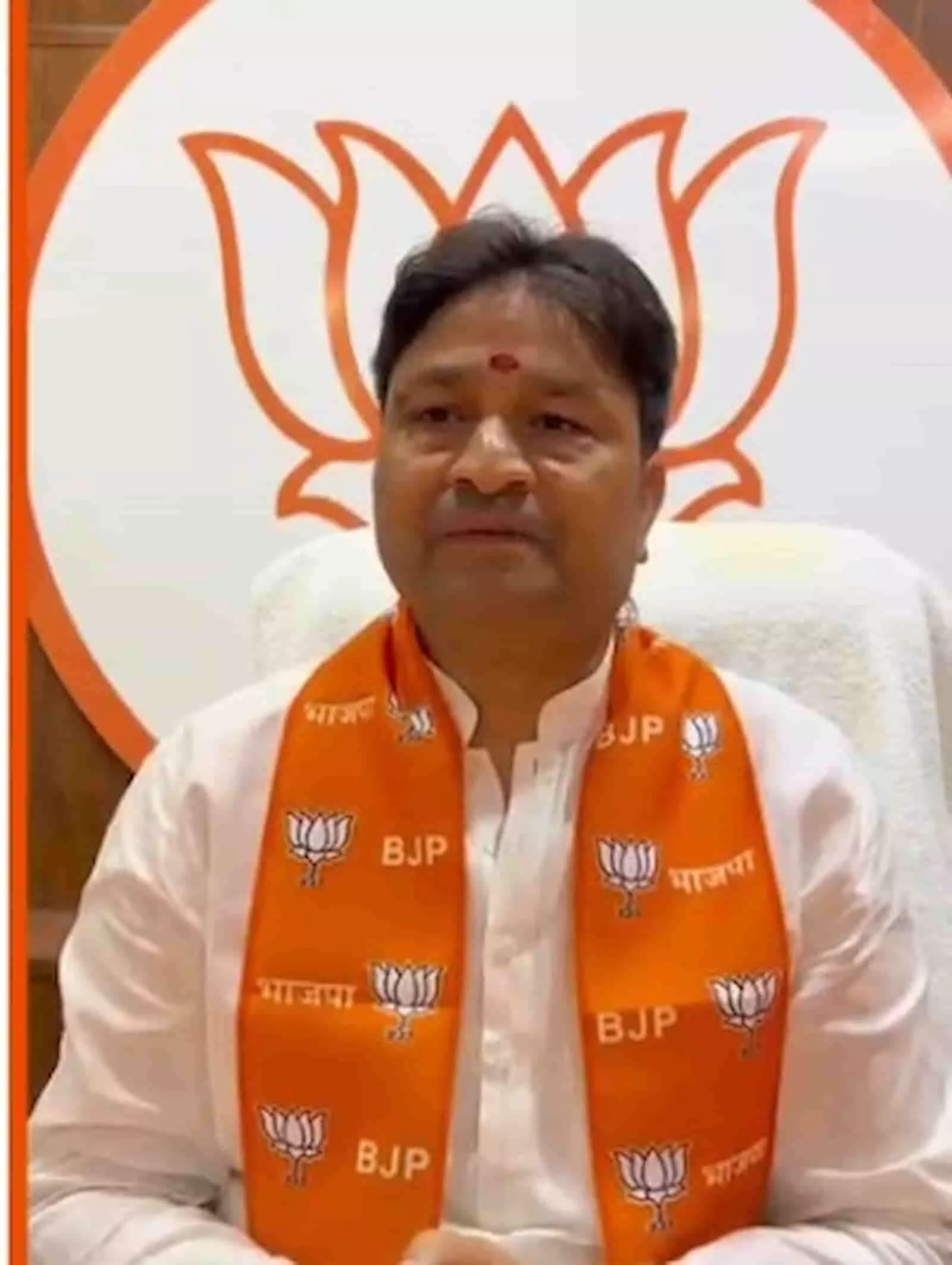 भगवा पटका पहने भाजपा प्रदेश महामंत्री भूपेंद्र सैनी जयपुर में पार्टी के बैकड्रॉप के सामने बैठकर प्रेस वार्ता करते हुए।