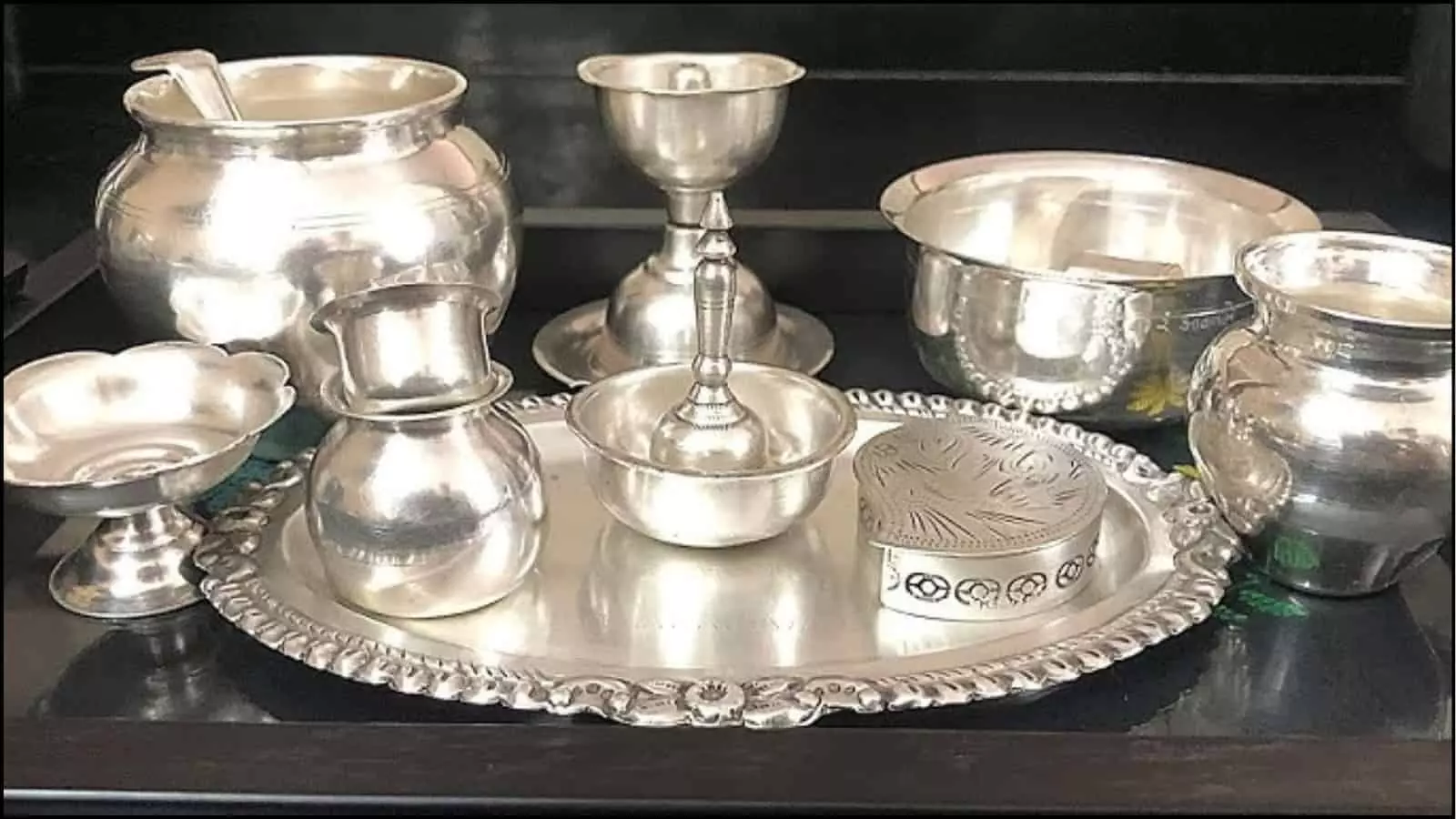 काली ट्रे के ऊपर रखे हुए चांदी के विभिन्न बर्तन और थाली सराफा बाजार की चांदी की दरों के संदर्भ में।