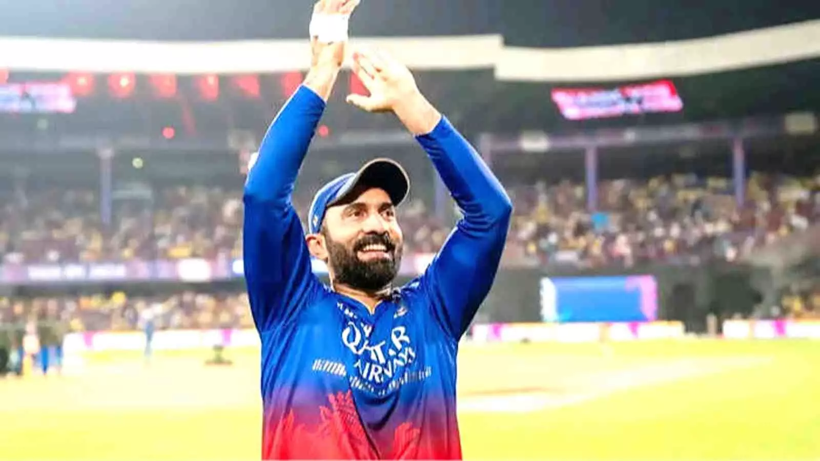 क्रिकेट स्टेडियम के मैदान पर खड़े दिनेश कार्तिक दर्शकों की ओर देखकर दोनों हाथ ऊपर उठाकर ताली बजा रहे हैं।