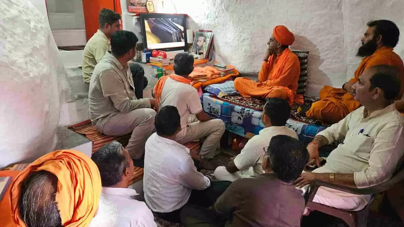 टीवी स्क्रीन पर प्रधानमंत्री मोदी का कार्यक्रम देखते हुए महंत प्रताप पुरी और अन्य लोग गुरु शिखर गुफा में बैठे हैं।