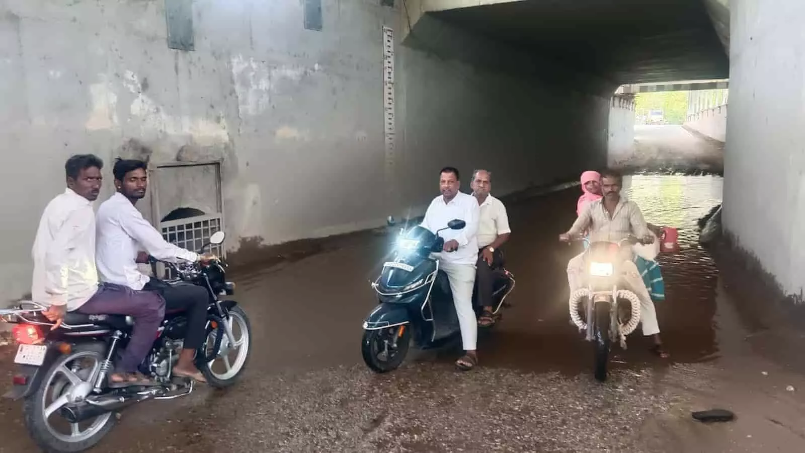 रेलवे अंडरपास के नीचे भरे पानी में मोटरसाइकिल निकालते हुए ग्रामीण पुरुष खेरोदा में जलभराव के संदर्भ में। रेलवे अंडरपास के नीचे भरे पानी में मोटरसाइकिल निकालते हुए ग्रामीण पुरुष खेरोदा में जलभराव के संदर्भ में।