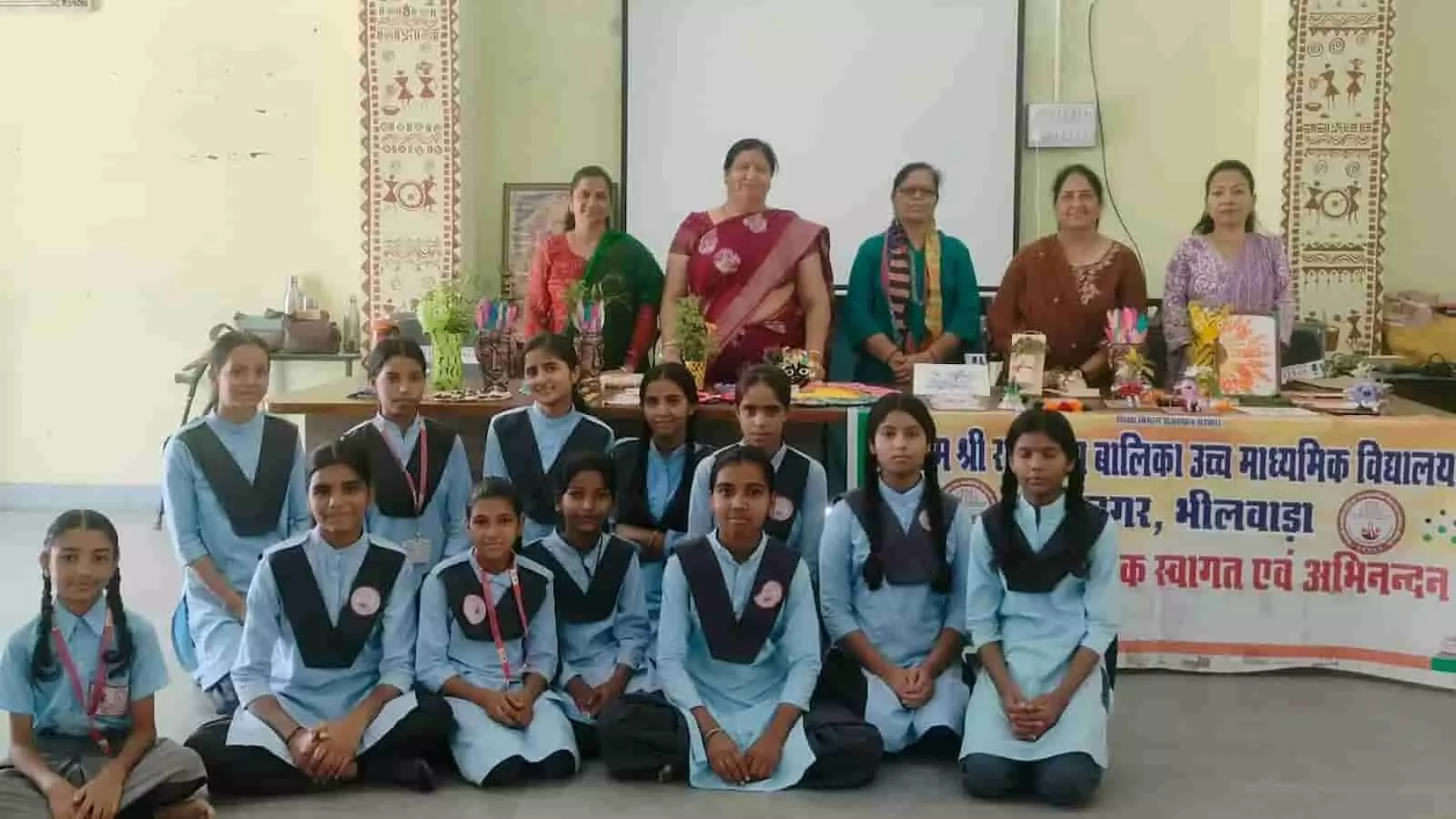 विद्यालय के कमरे में शिक्षिकाएं और छात्राएं हस्तनिर्मित कलाकृतियों के साथ समूह चित्र के लिए बैठी हैं। विद्यालय के कमरे में शिक्षिकाएं और छात्राएं हस्तनिर्मित कलाकृतियों के साथ समूह चित्र के लिए बैठी हैं।