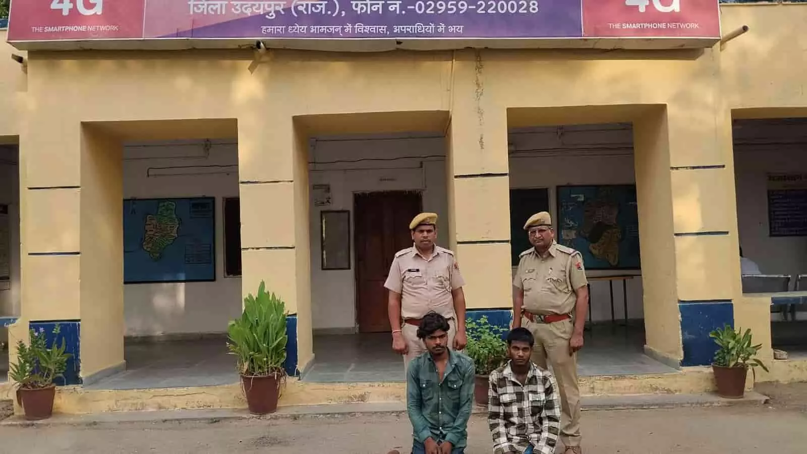 झाडोल पुलिस थाने के सामने दो पुलिसकर्मियों के साथ घुटनों के बल बैठे लूट के दो आरोपी।