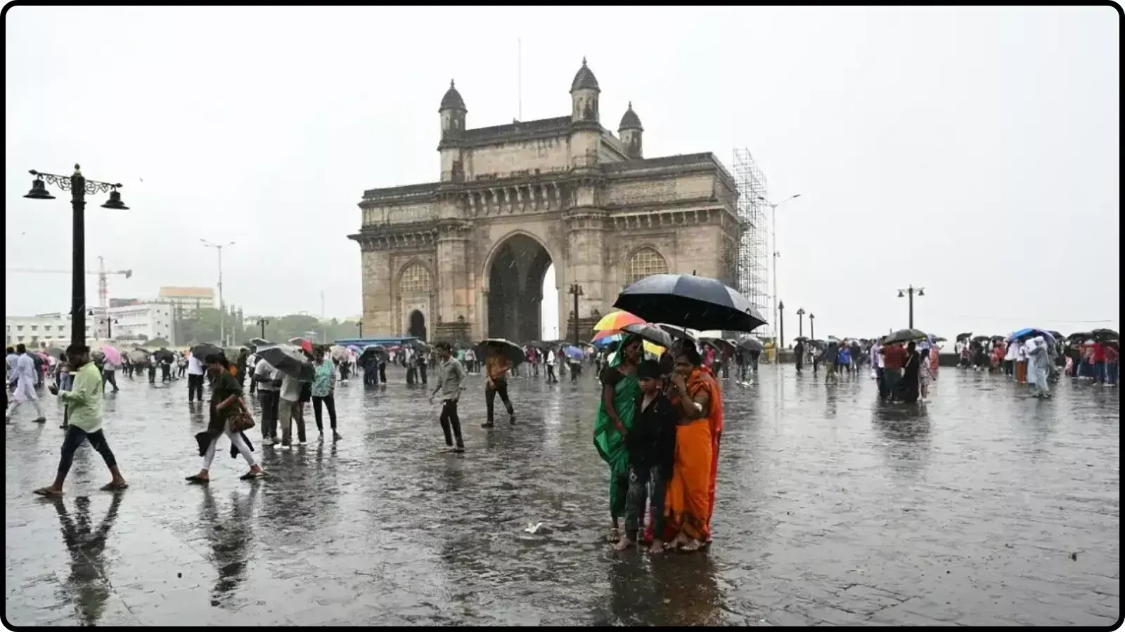 बारिश के बीच छाता लिए खड़े लोग गेटवे ऑफ इंडिया मुंबई में मौसम परिवर्तन के संदर्भ में।