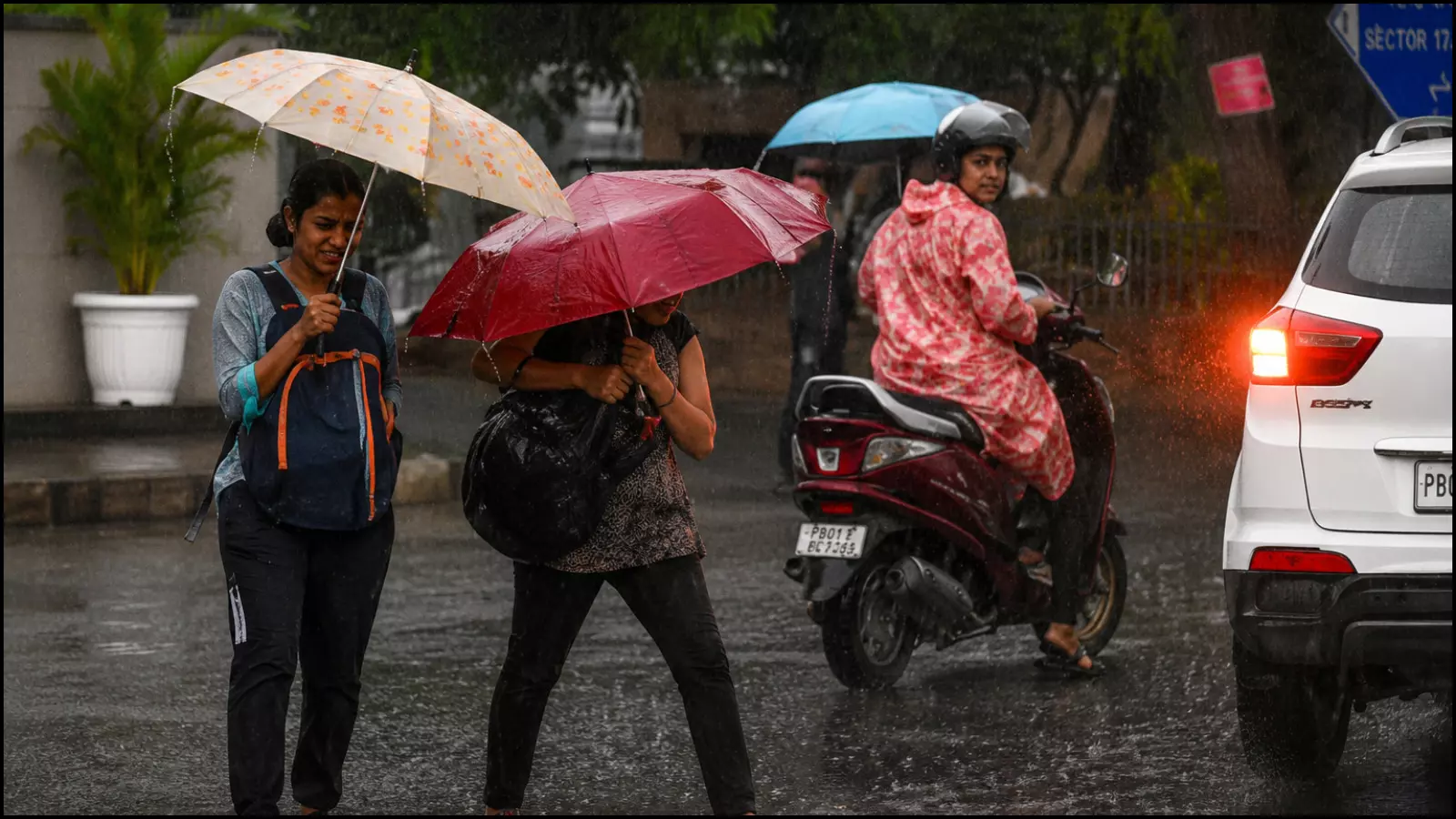 तेज बारिश के बीच छाता लेकर सड़क पार करतीं महिलाएं और दोपहिया वाहन चालक। तेज बारिश के बीच छाता लेकर सड़क पार करतीं महिलाएं और दोपहिया वाहन चालक।