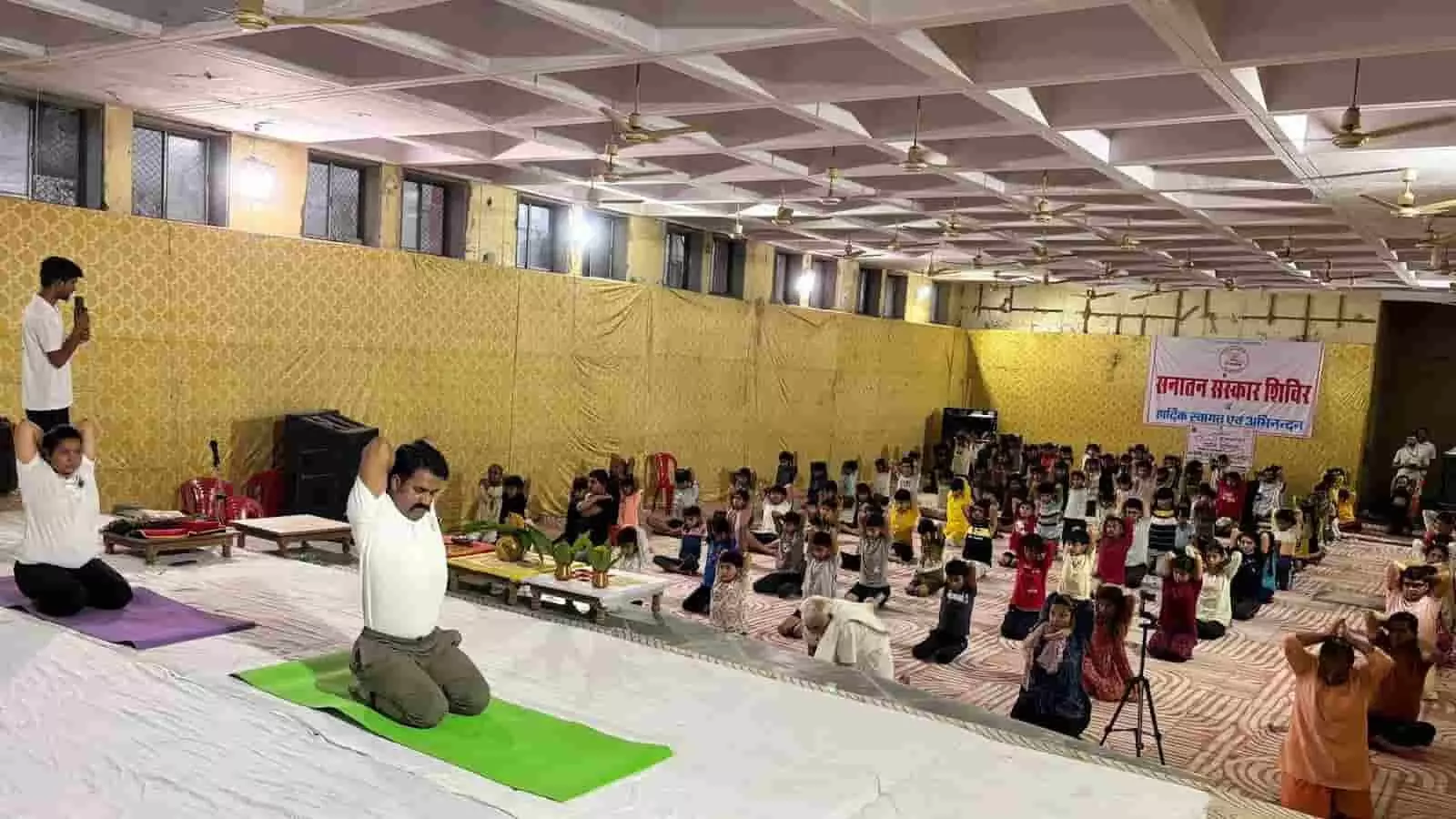 सांवरिया विश्राम गृह के हॉल में योग प्रशिक्षक और बच्चे योगासन का अभ्यास कर रहे हैं।
