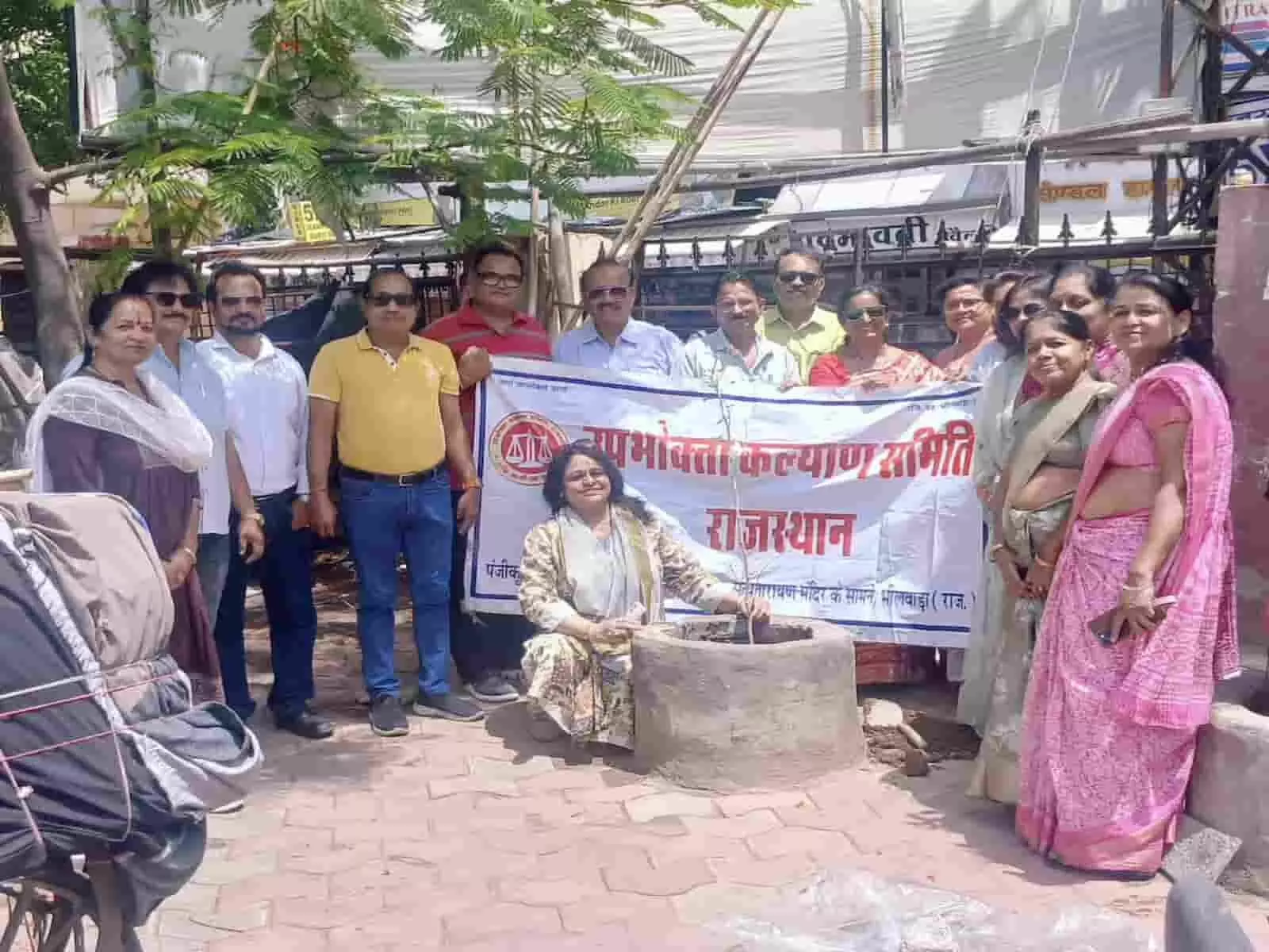 भीलवाड़ा के आजाद चौक में बैनर के पीछे खड़े उपभोक्ता कल्याण समिति के पदाधिकारी पौधा लगाते हुए।