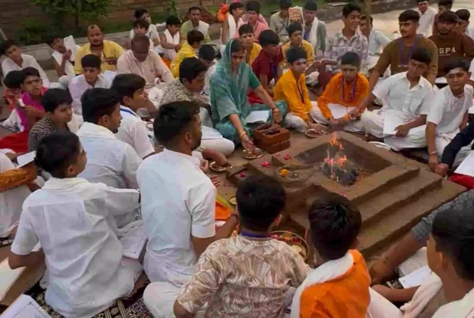 यज्ञ कुंड के चारों ओर बैठकर धार्मिक पुस्तकें थामे वैदिक विधि से हवन करते हुए बच्चे और नागरिक चित्तौड़गढ़ शिविर में।