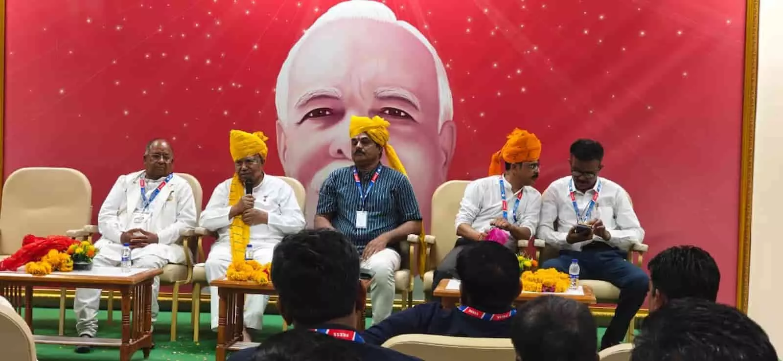 तस्वीर में मंच पर बैठे IFWJ के वरिष्ठ पदाधिकारी और कार्यक्रम में उपस्थित पत्रकार।