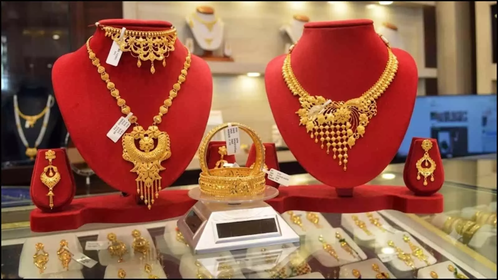 शोरूम के काउंटर पर लाल डिस्प्ले स्टैंड पर सजे हुए सोने के भारी आभूषण और हार रखे हुए हैं शोरूम के काउंटर पर लाल डिस्प्ले स्टैंड पर सजे हुए सोने के भारी आभूषण और हार रखे हुए हैं