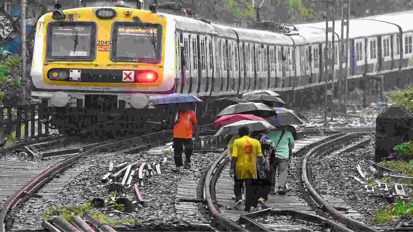 बारिश के मौसम में पटरी पर छतरी लेकर चलते लोग और सामने आती ट्रेन|