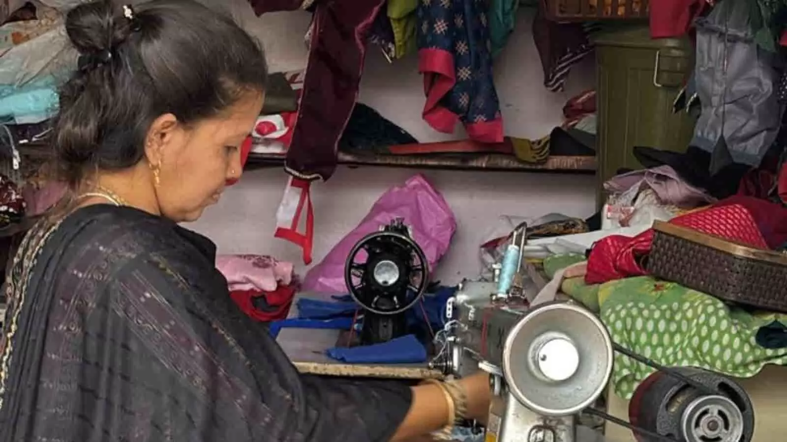 सिलाई मशीन पर काम करती महिला और पृष्ठभूमि में टंगे कपड़े जो जिगर नायक की मां के संघर्ष को दर्शाते हैं। सिलाई मशीन पर काम करती महिला और पृष्ठभूमि में टंगे कपड़े जो जिगर नायक की मां के संघर्ष को दर्शाते हैं।