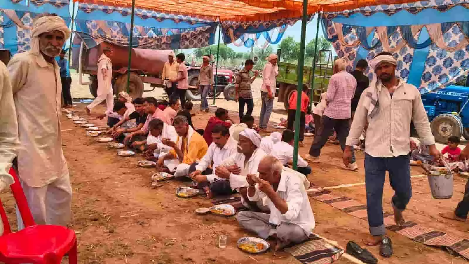 मन्नापुर गांव के हीरामन बाबा स्थान पर टेंट के नीचे जमीन पर बैठकर भोजन करते ग्रामीण पुरुष।