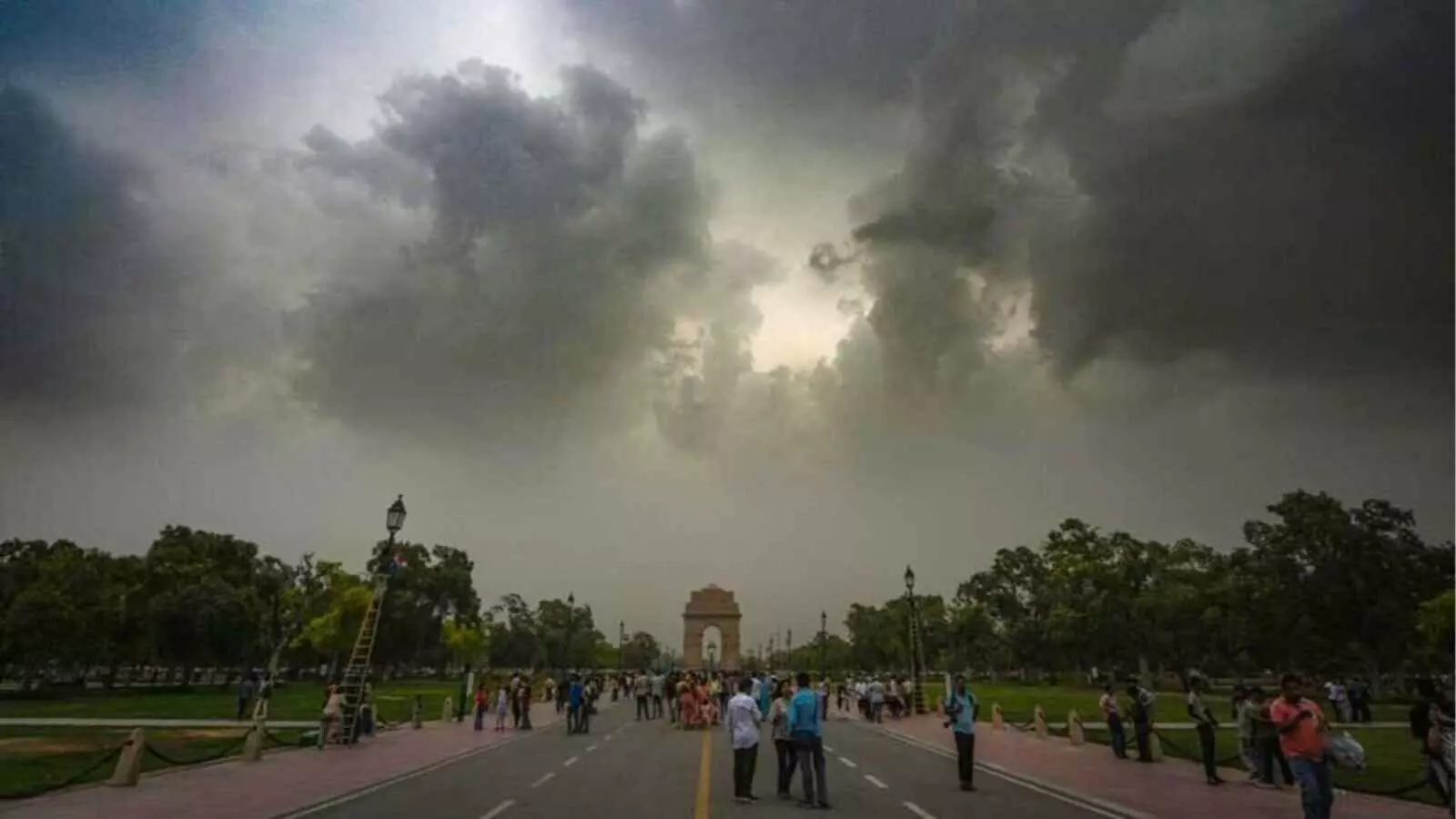 काले बादल और धूल भरे आसमान के नीचे इंडिया गेट राजपथ पर घूमते लोग|