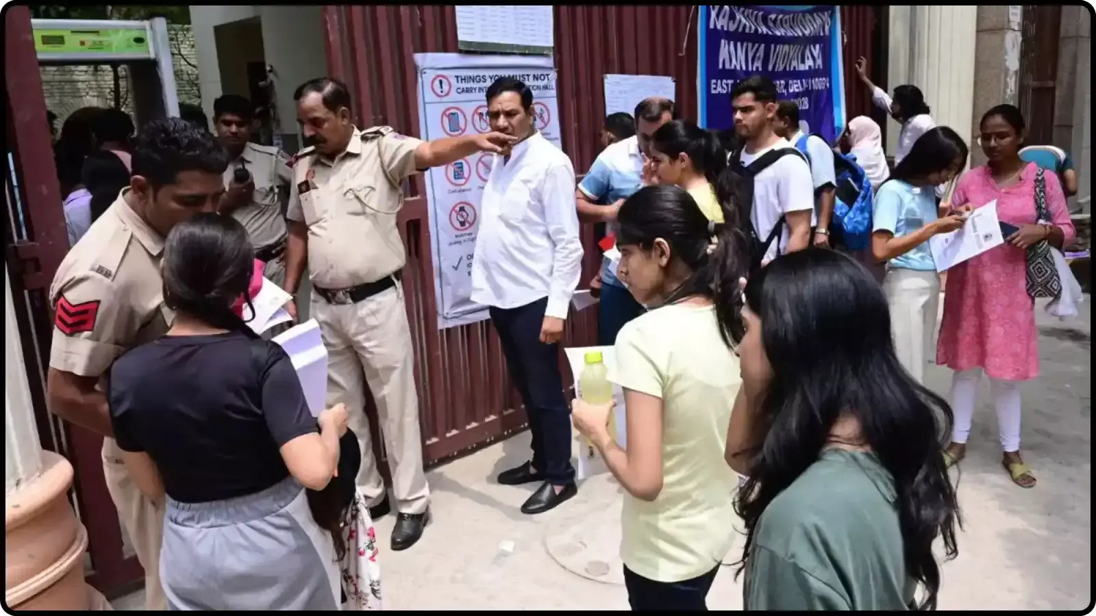 परीक्षा केंद्र के प्रवेश द्वार पर एडमिट कार्ड दिखाते अभ्यर्थी और सुरक्षा जांच करते पुलिसकर्मियों की तस्वीर।