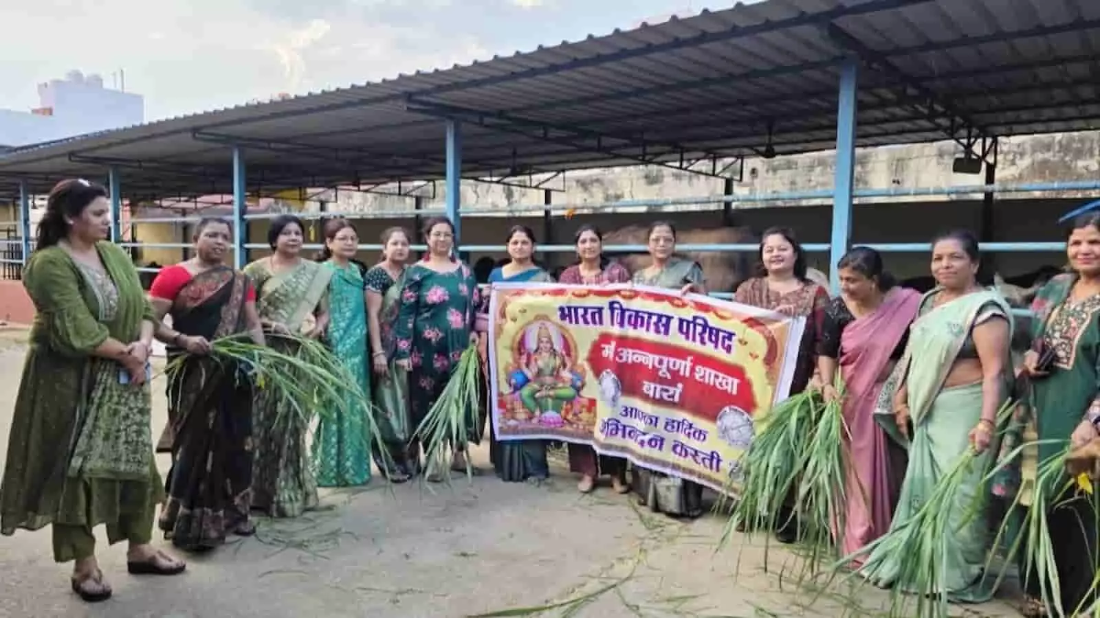 बारां में भारत विकास परिषद की महिला सदस्य बैनर लेकर गौशाला में चारे के साथ खड़ी हैं।