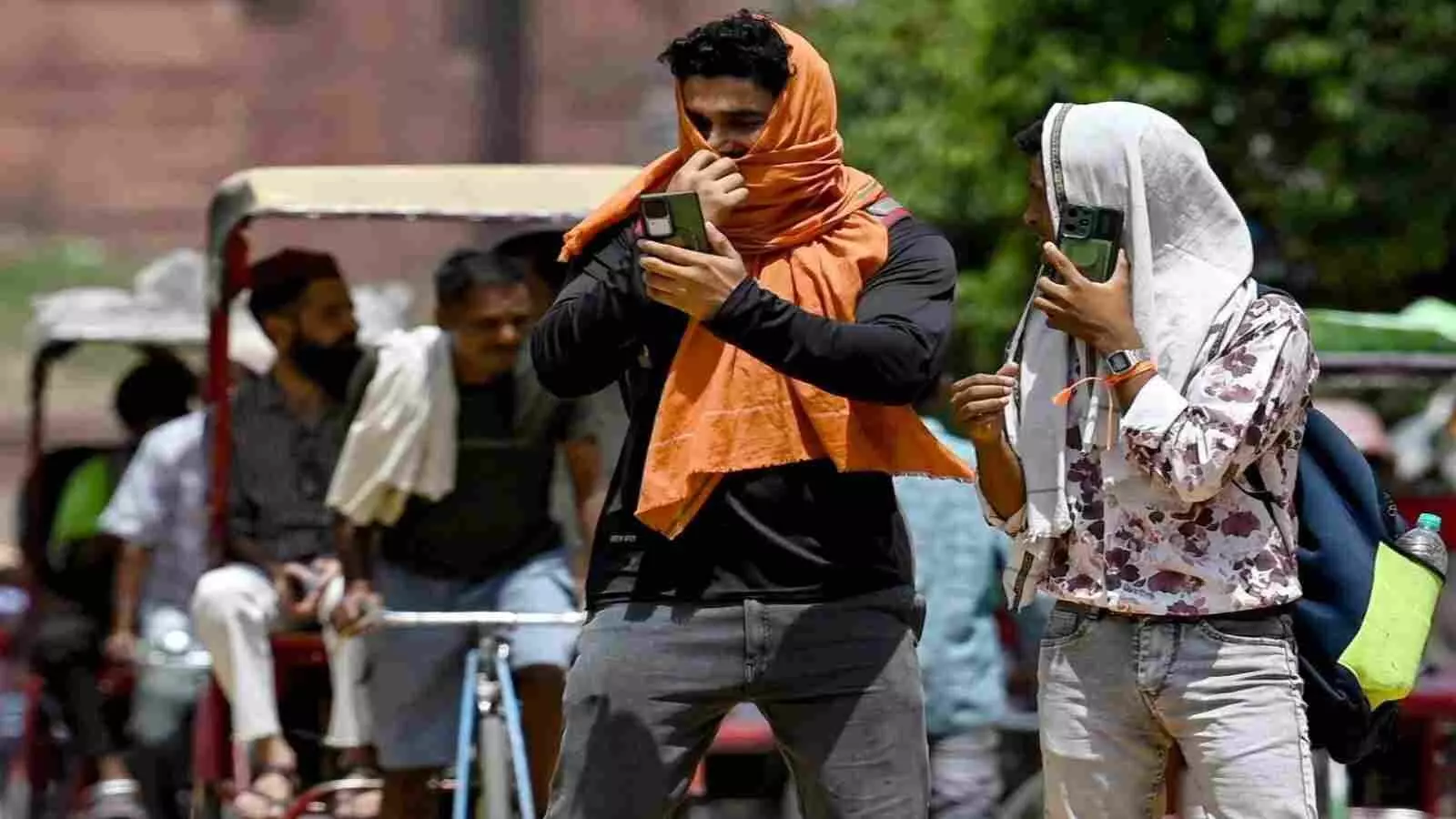 दिल्ली की धूप में चेहरे को सूती कपड़े से ढककर मोबाइल फोन देखते दो पुरुष राहगीर। दिल्ली की धूप में चेहरे को सूती कपड़े से ढककर मोबाइल फोन देखते दो पुरुष राहगीर।