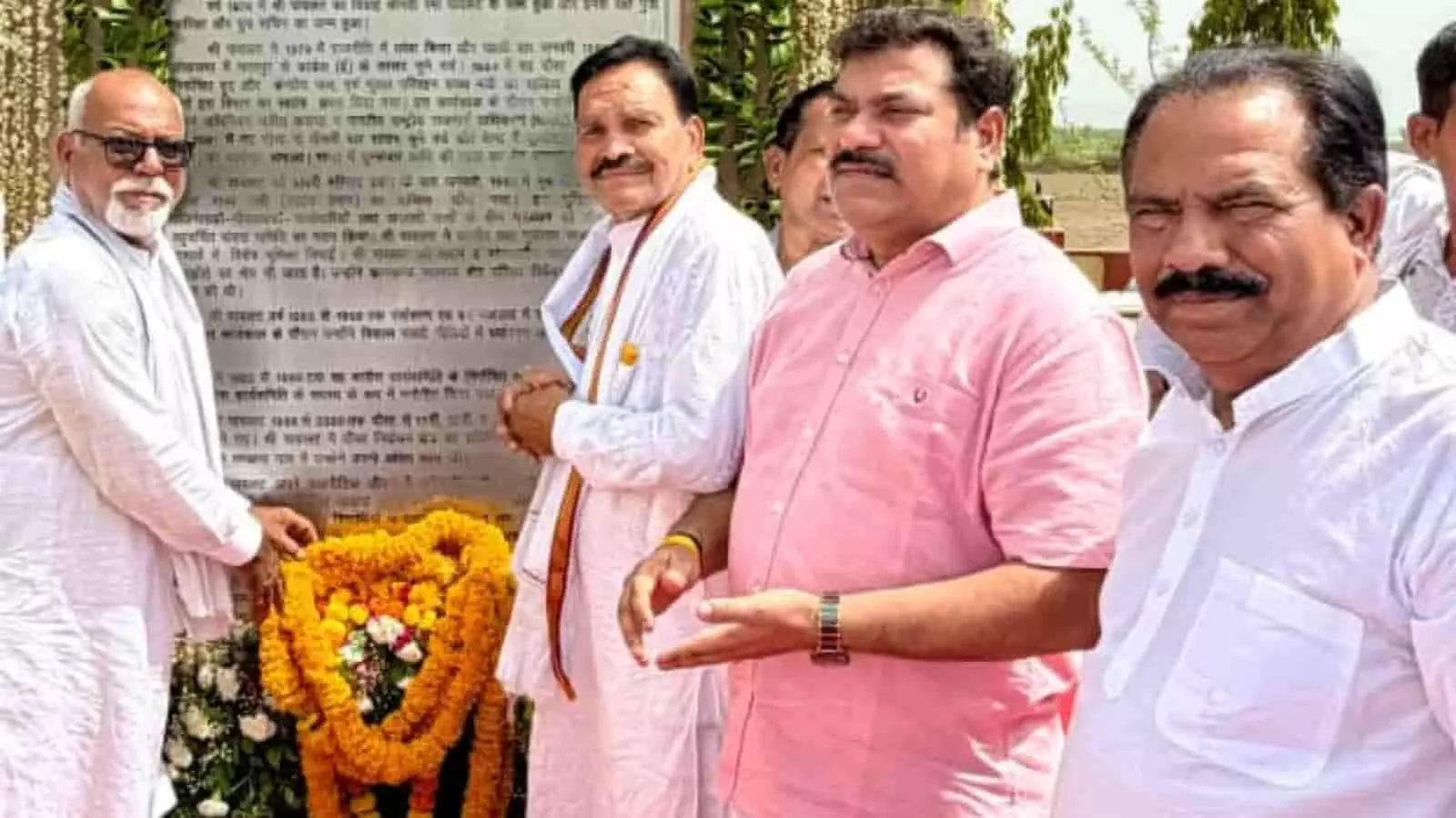 तस्वीर में कुछ लोग एक स्मृति स्थल पर माला चढ़ाने के बाद हाथ जोड़कर खड़े दिखाई दे रहे हैं।