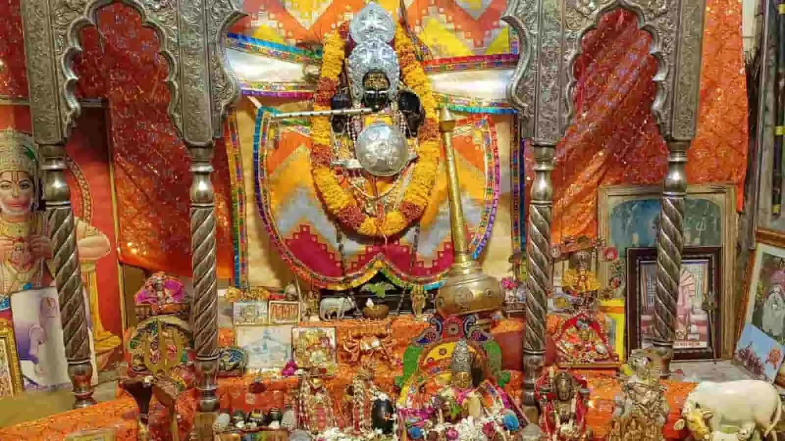 तस्वीर में एक मंदिर के भीतर भगवान श्रीकृष्ण की सुंदर प्रतिमा और पूजा की सामग्री दिखाई दे रही है।