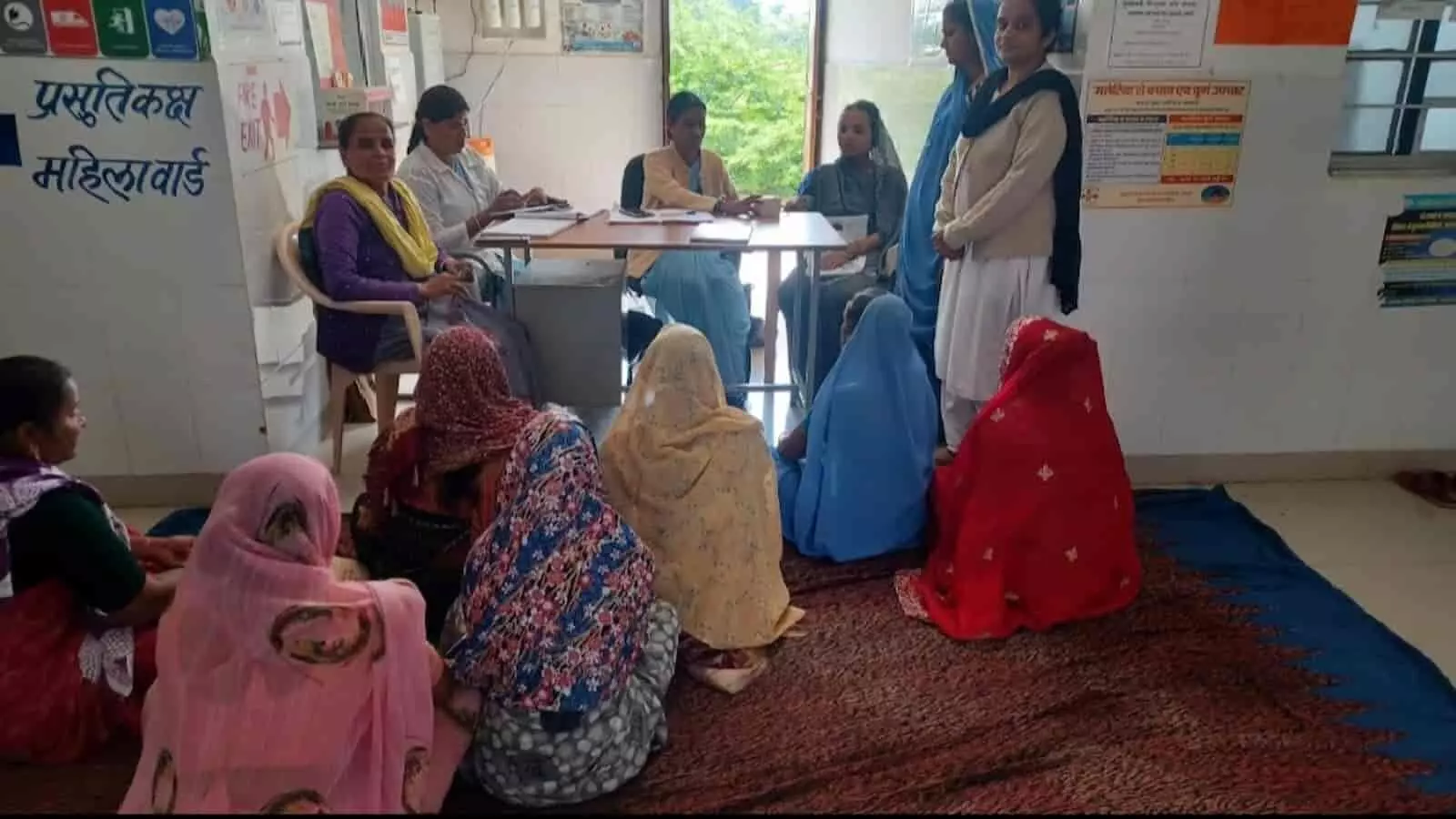 तस्वीर में प्रसूति कक्ष और महिला वार्ड के बाहर जमीन पर बैठी महिलाएं टेबल पर मौजूद चिकित्सा कर्मियों से परामर्श ले रही हैं। तस्वीर में प्रसूति कक्ष और महिला वार्ड के बाहर जमीन पर बैठी महिलाएं टेबल पर मौजूद चिकित्सा कर्मियों से परामर्श ले रही हैं।